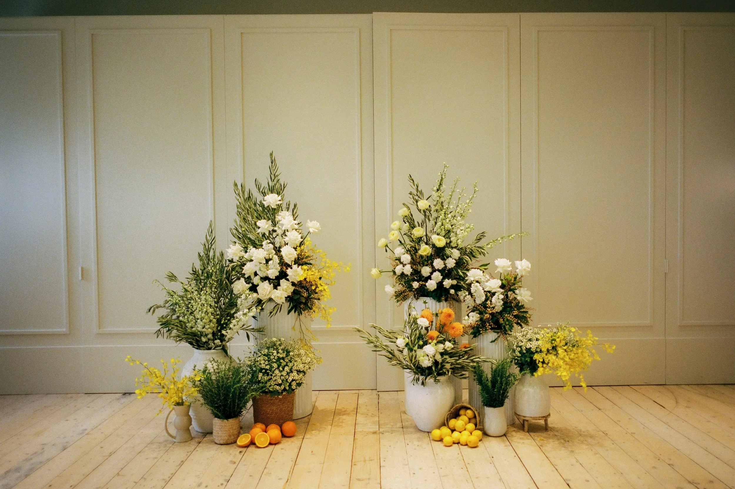 InterContinental Sorrento wedding styling by Poppy Culture with vibrant citrus accents and modern white‑and‑yellow florals arranged in layered vessels.