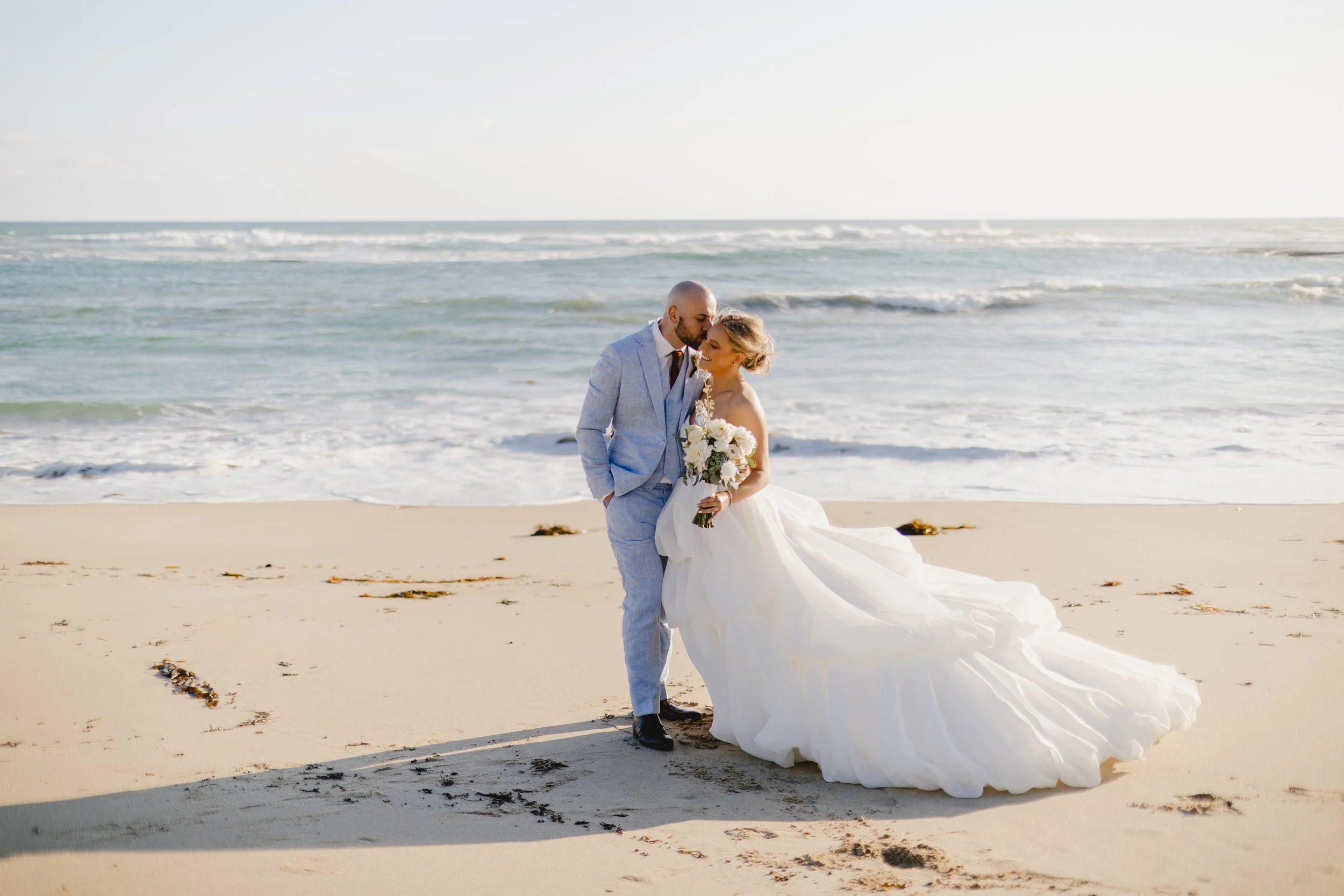 All Smiles Sorrento beach wedding with the couple standing by the shoreline and the bride holding a Poppy Culture bouquet.