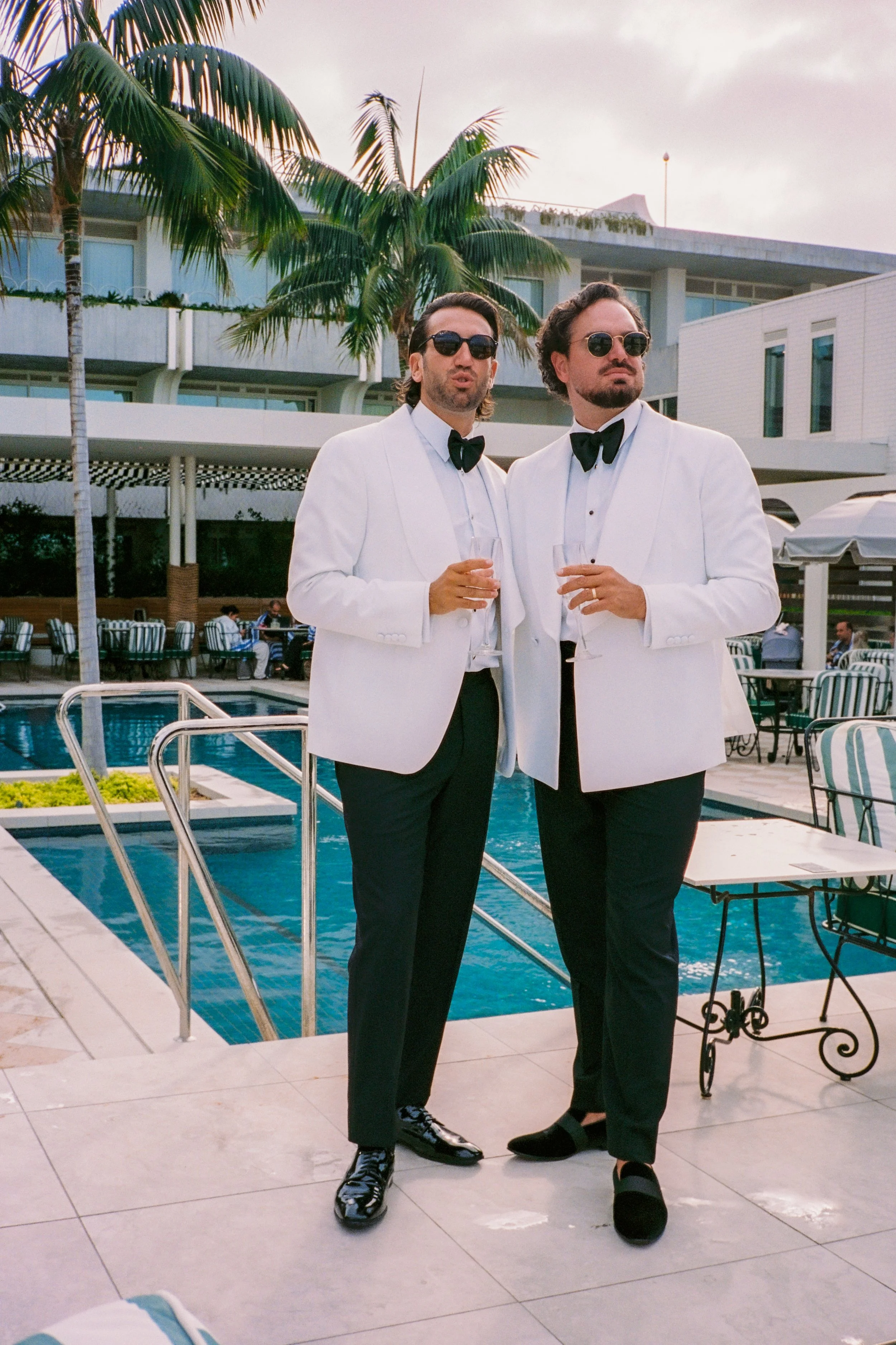 Poolside scene at InterContinental Sorrento featuring two grooms in white tuxedos. Coastal palms in the background.