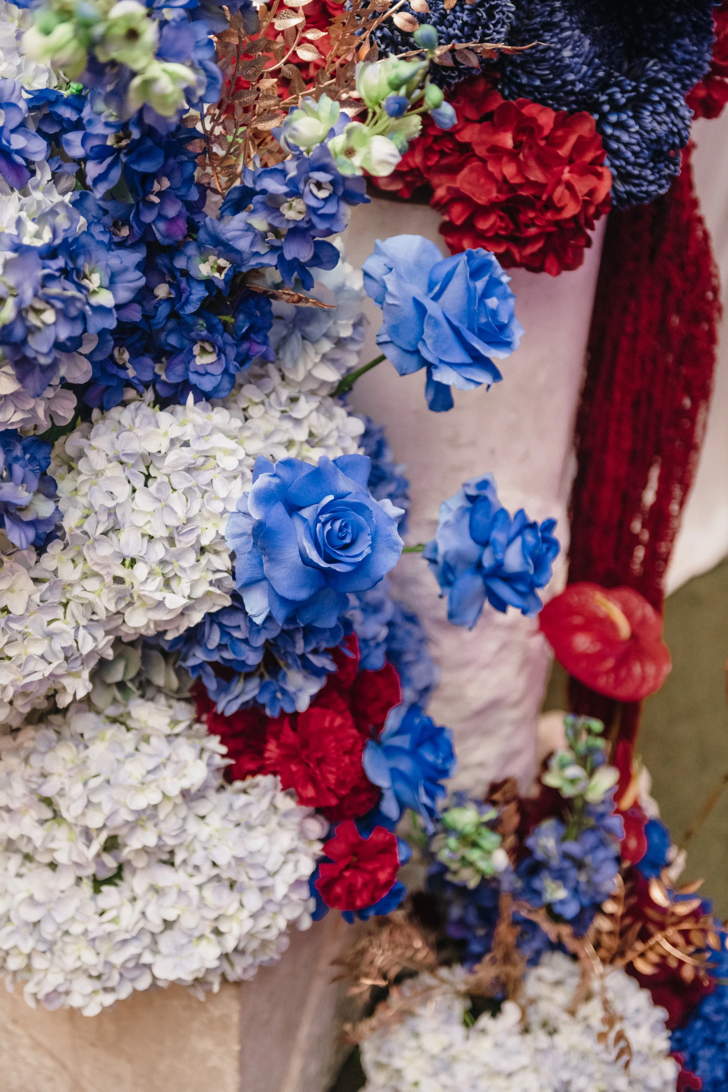 Modern‑lux corporate event styling by Poppy Culture at RACV Cape Schanck Resort, featuring a detailed floral installation in a blue, red and white palette. Blue roses, blue hydrangeas, red anthuriums, red textured blooms, white florals and dried gold