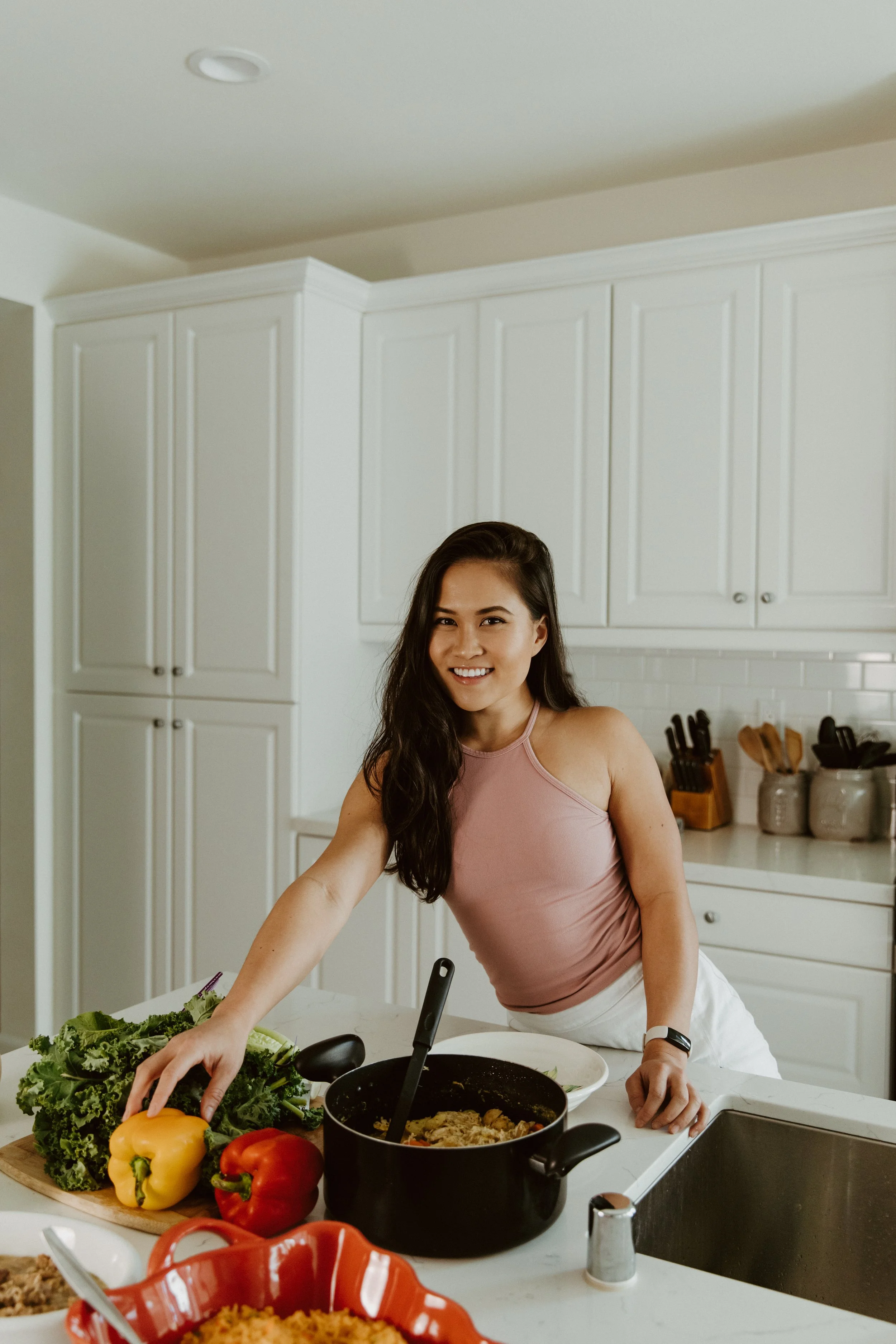 Woman smiling in a kitchen with vegetables and a pot of cooked food on the counter.