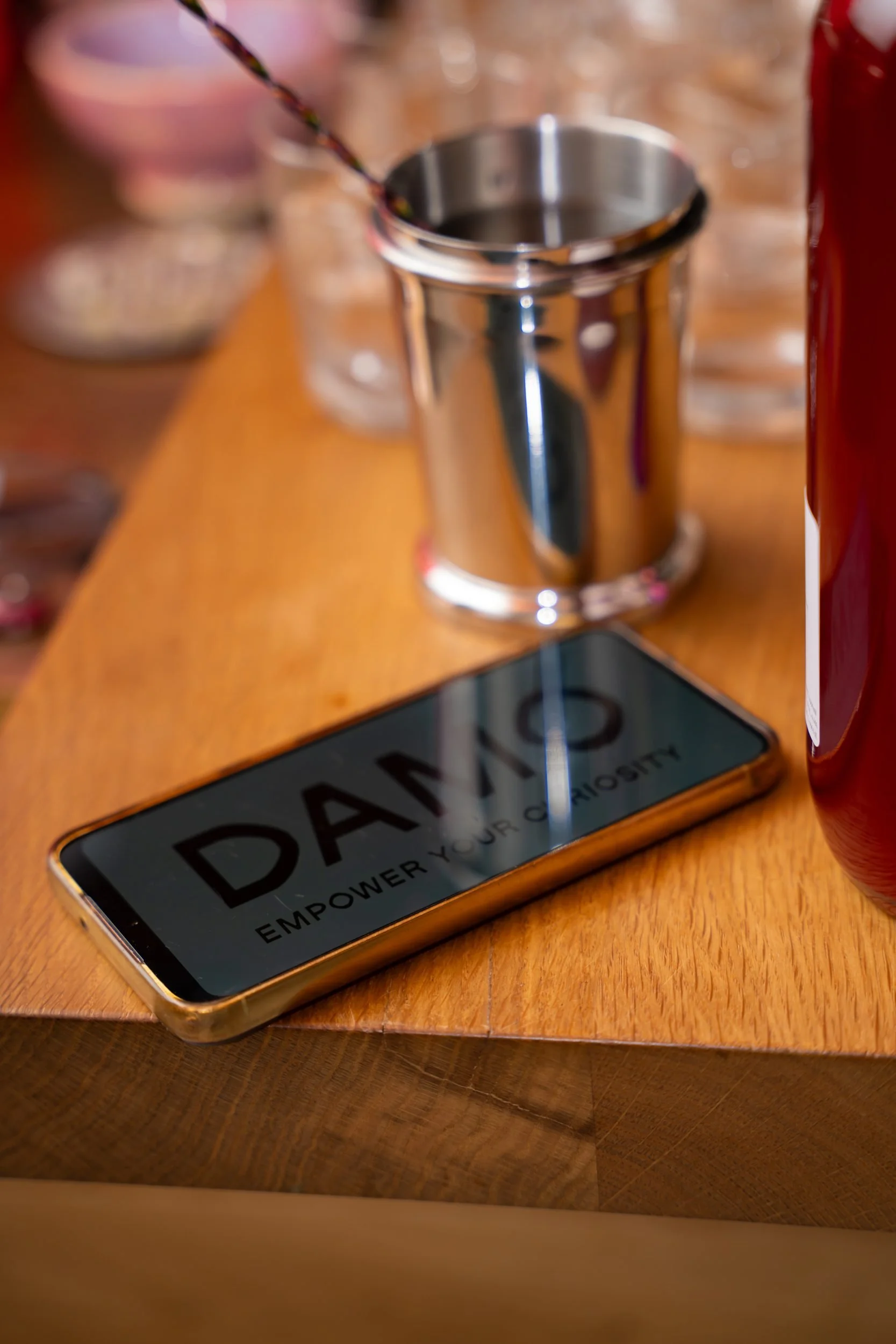 Phone showing the DAMO logo on the wooden bar next to a steel jigger at the Copenhagen Fashion Week SS26 Opening Reception