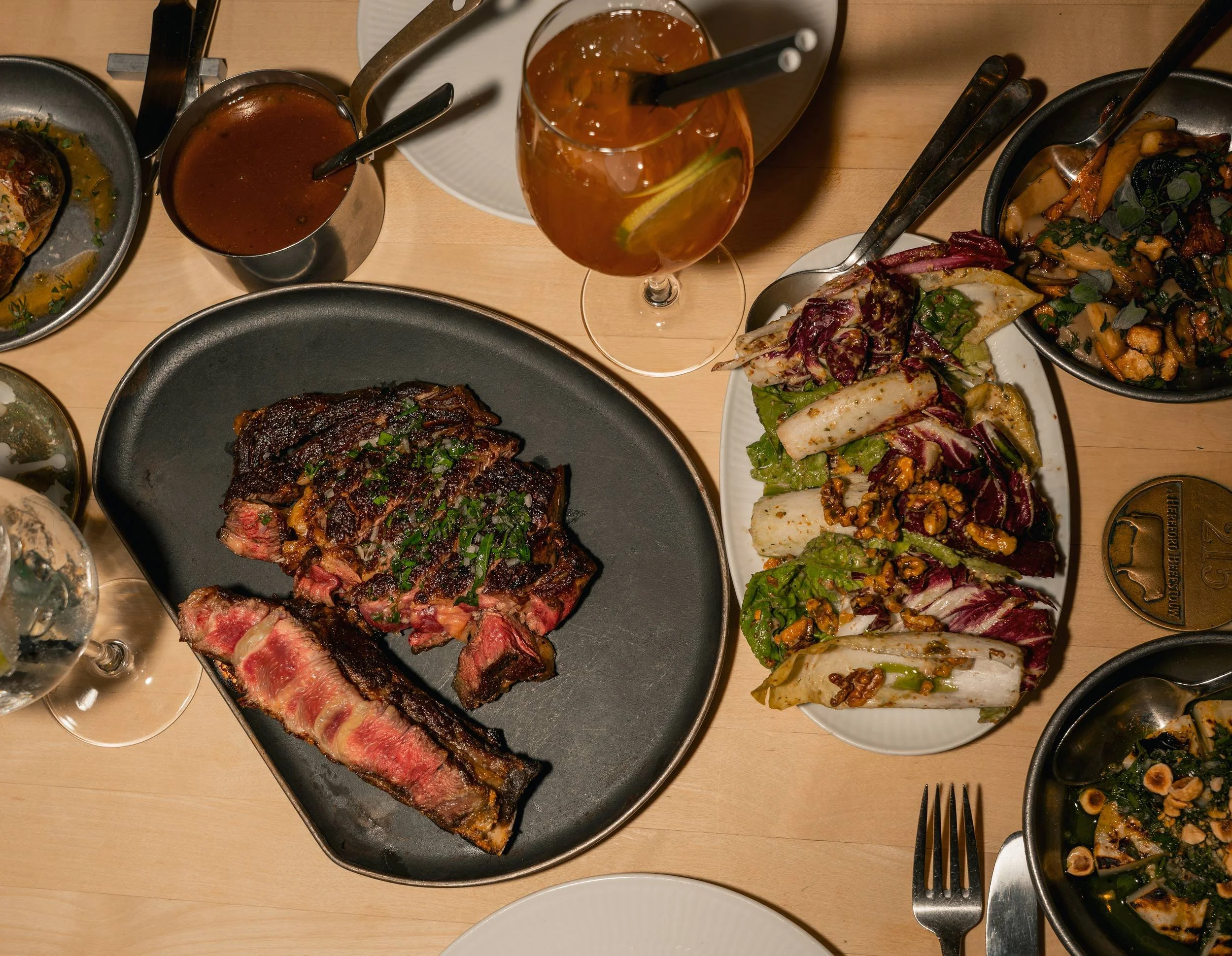 Bord ovenfra med skåret bøf, salat, tilbehør og saucer hos A Hereford Beefstouw