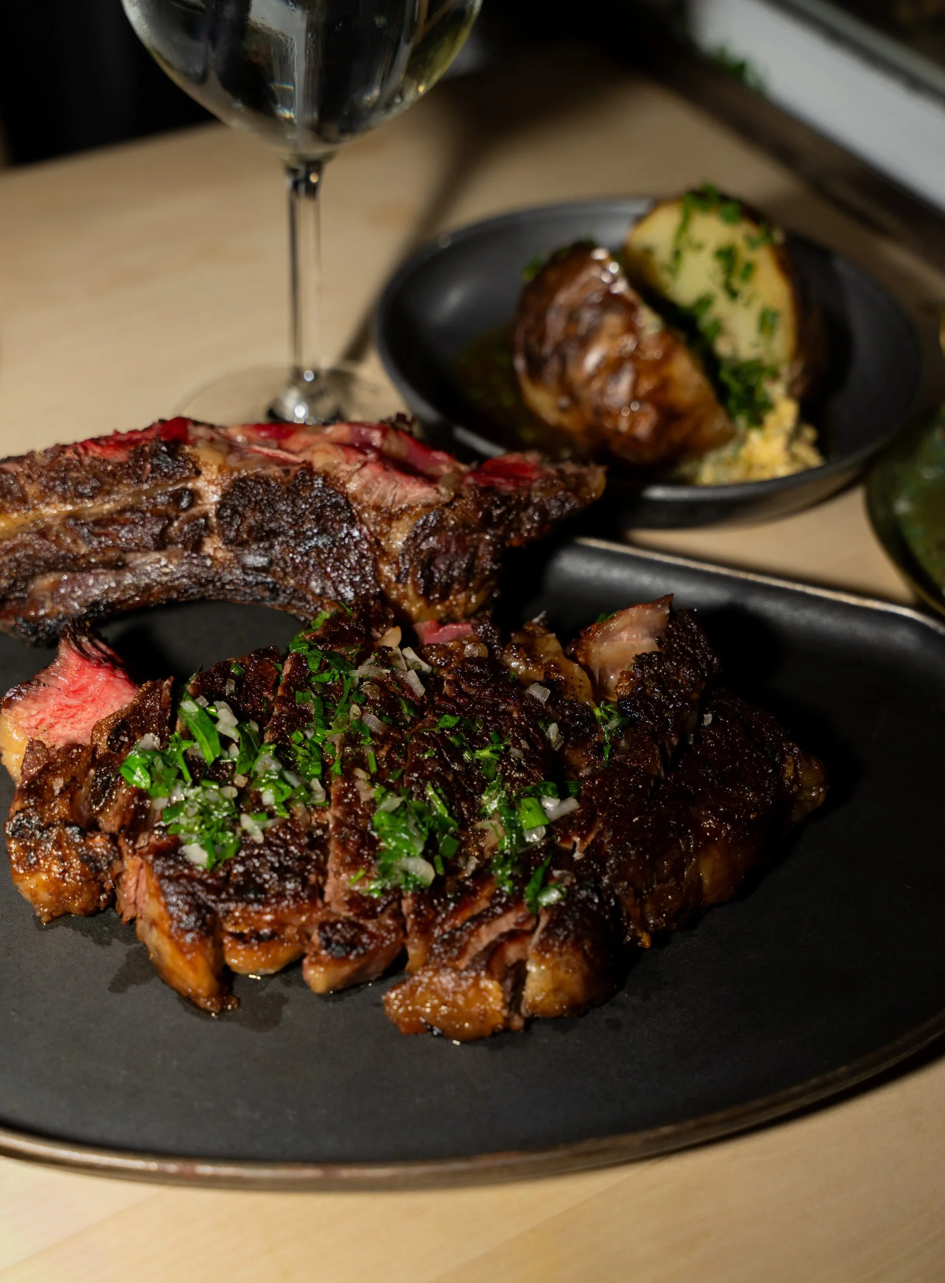 Grillet bøf med ben og krydderurter på sort tallerken med et glas vin hos A Hereford Beefstouw