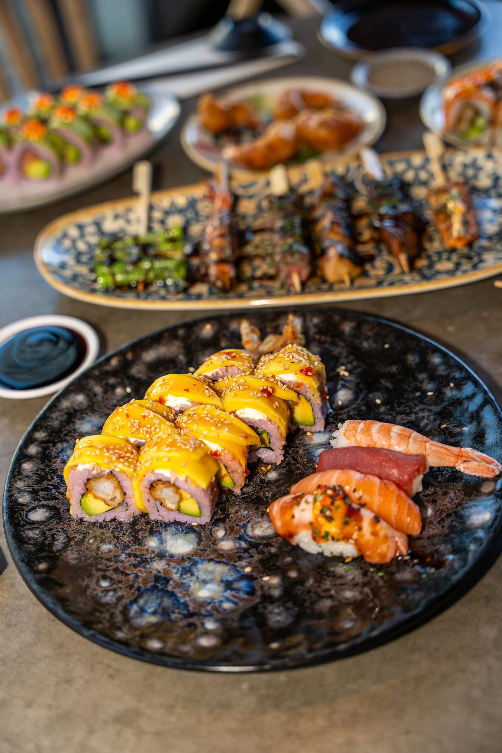 Maki-ruller og nigiri på sort stenfad foran et fad med grillede sticks hos Sushi Lab København