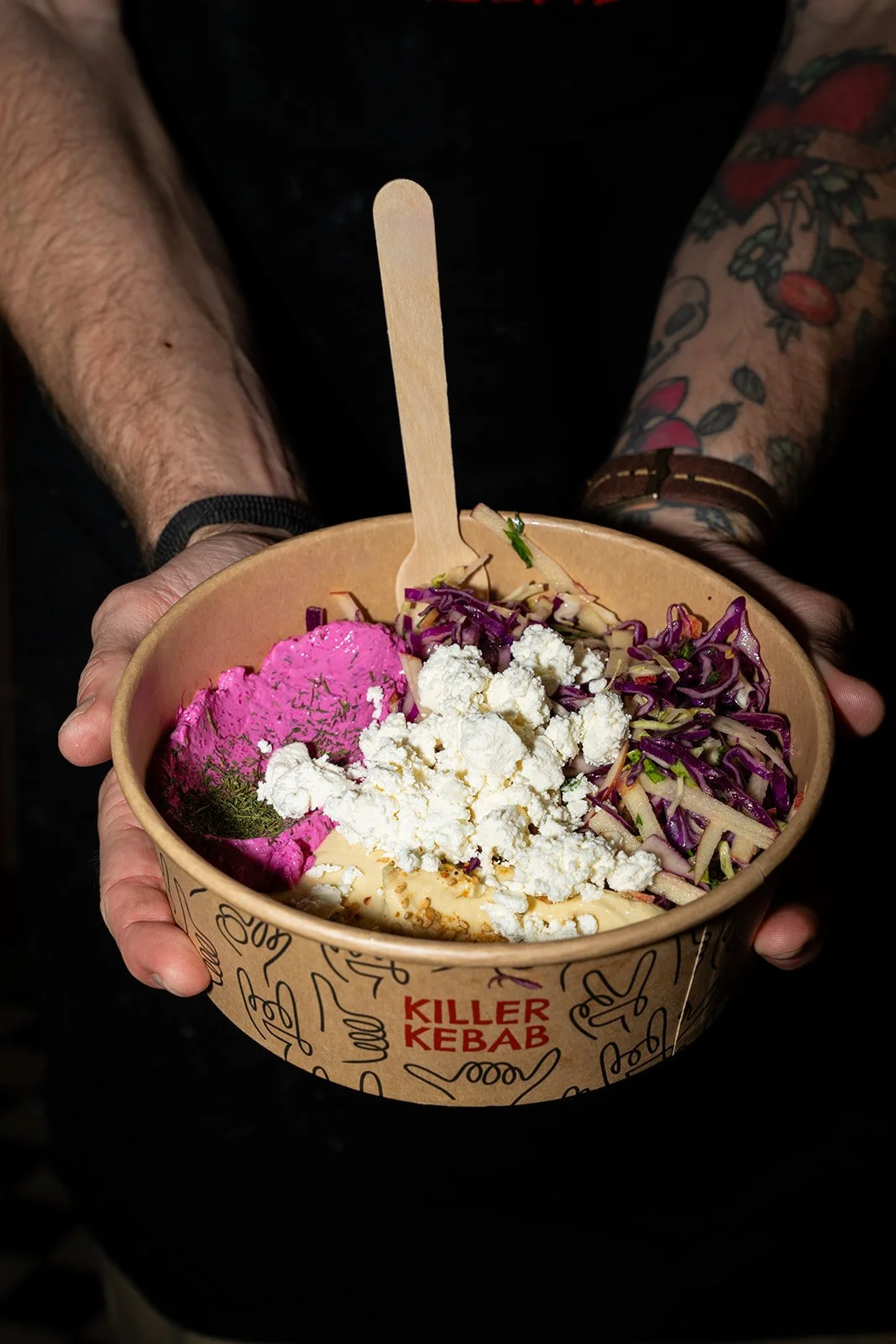 Bowl med pink hummus, feta og rødkål holdes frem i to hænder hos Killer Kebab