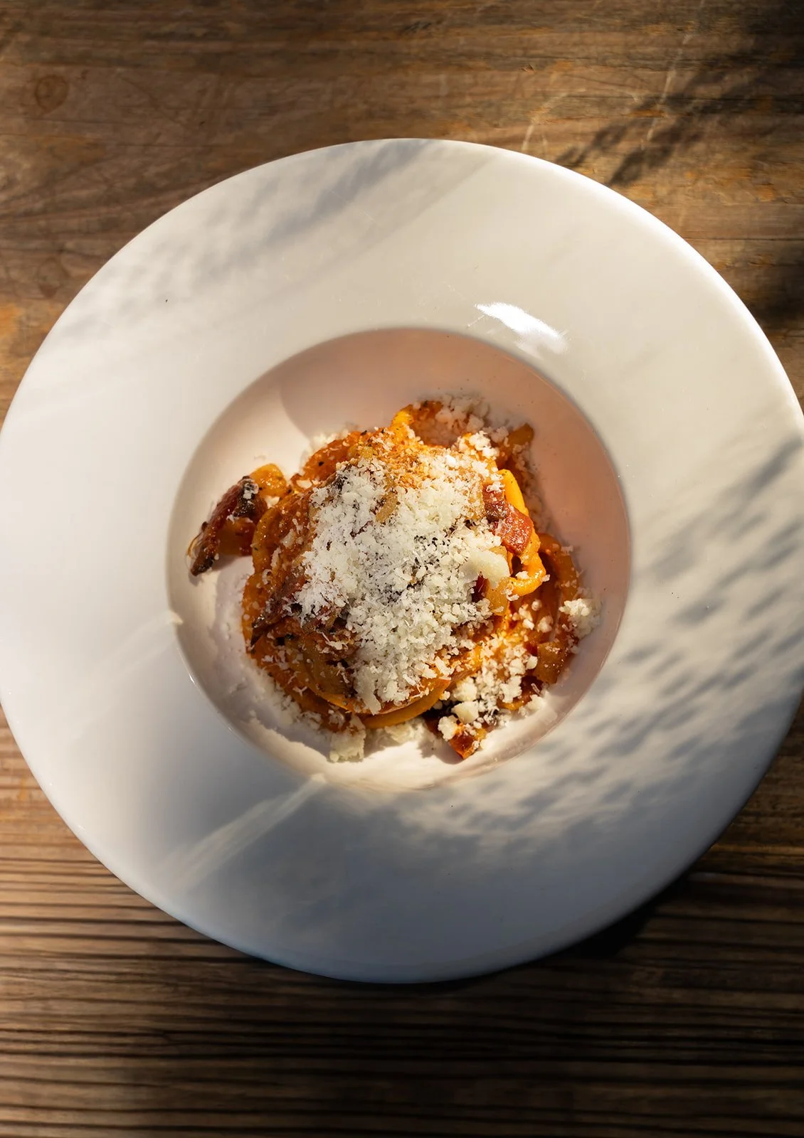 Pasta all'amatriciana med revet pecorino i en dyb hvid tallerken på et træbord hos Il Mattarello