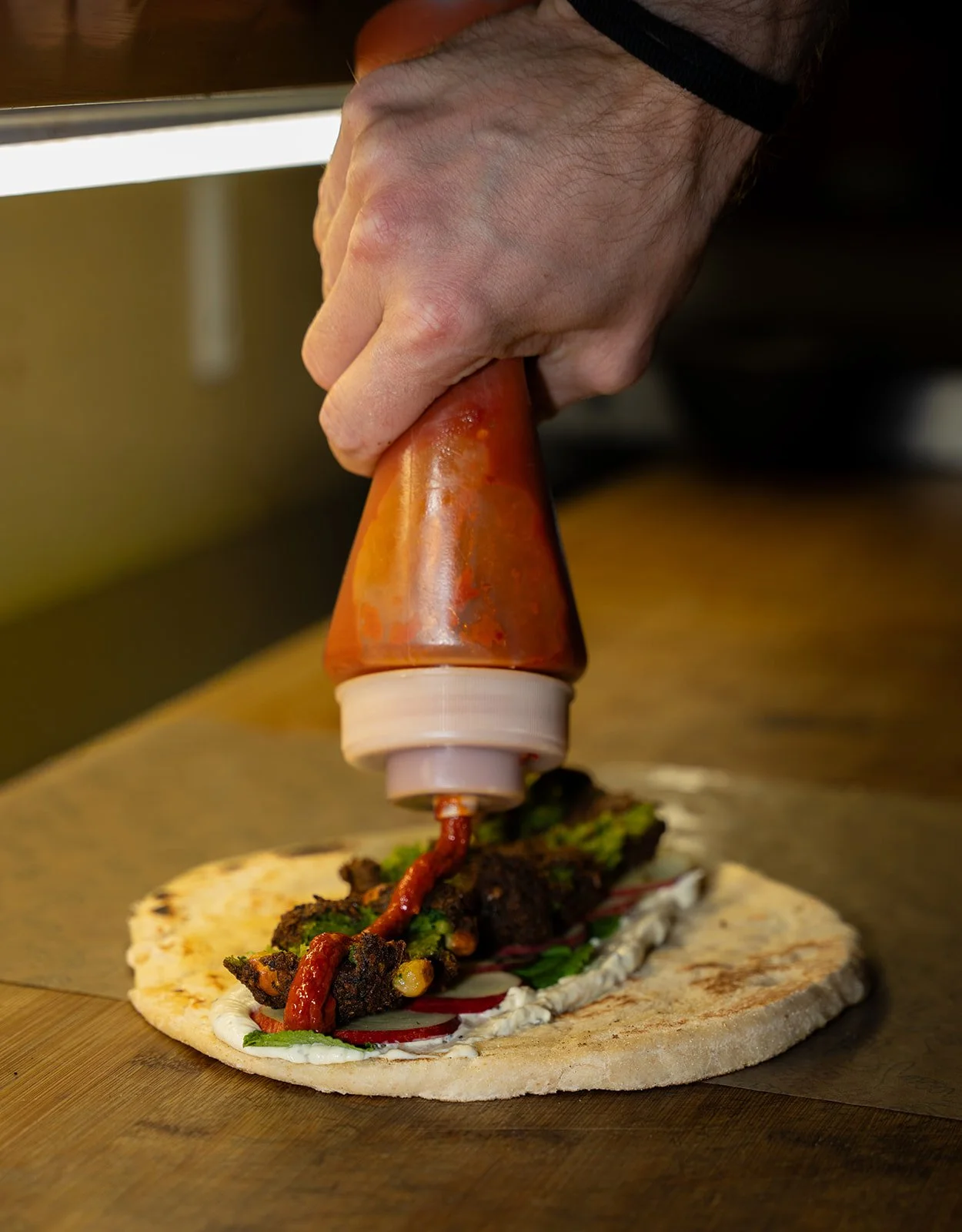 Sauce klemmes ud over kød og grøntsager på et fladbrød hos Killer Kebab