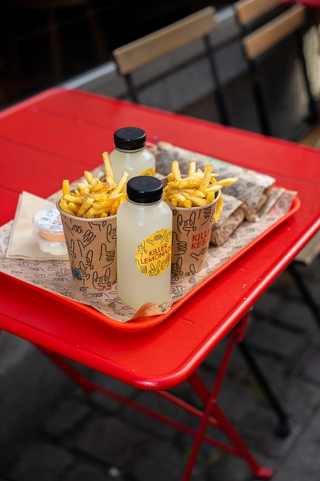 Bakke med kebabruller, pommes frites og lemonade på et rødt bord udenfor Killer Kebab