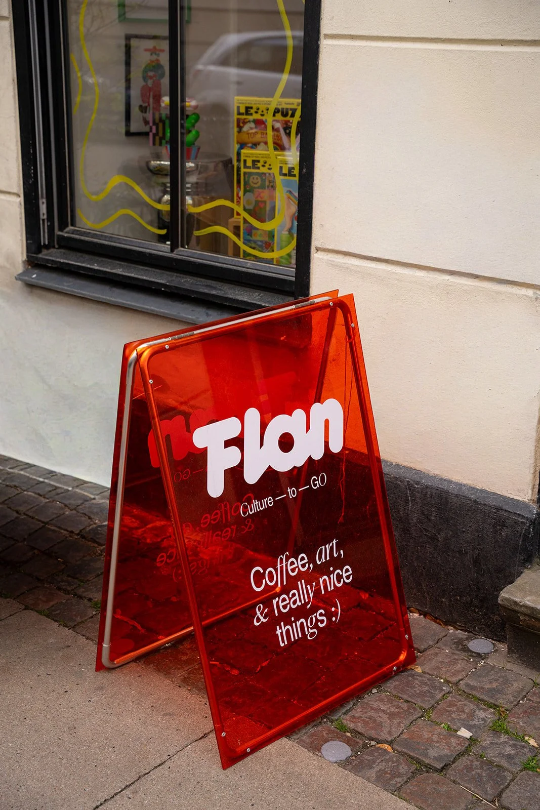 Rødt gadeskilt med Flan-logo på fortovet foran caféen på Vesterbro