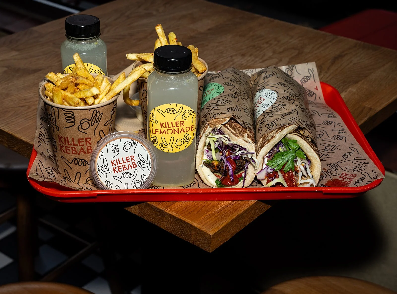 Rød bakke med kebabruller, pommes frites og lemonade på et træbord hos Killer Kebab