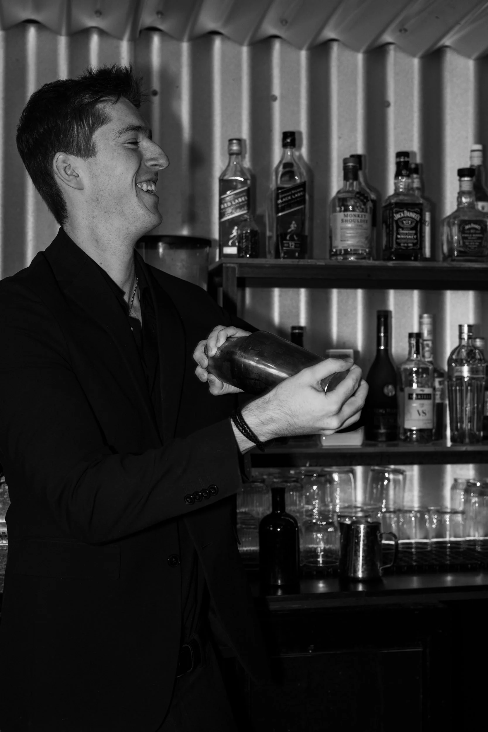 Bartender ryster en cocktail foran baglyste flaskehylder på Little Green Door