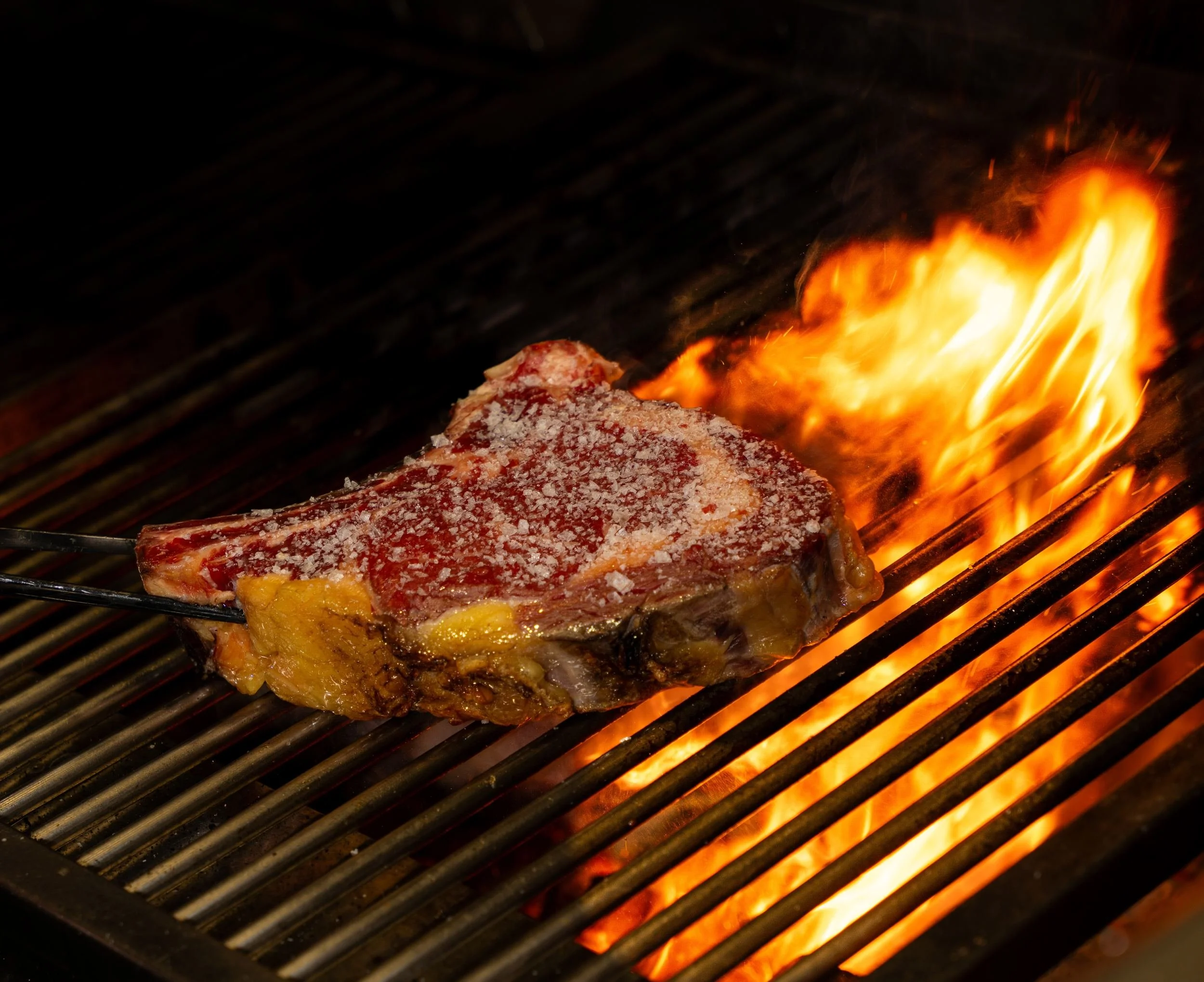 Bøf med ben på grillen med flammer, der slår op, hos A Hereford Beefstouw