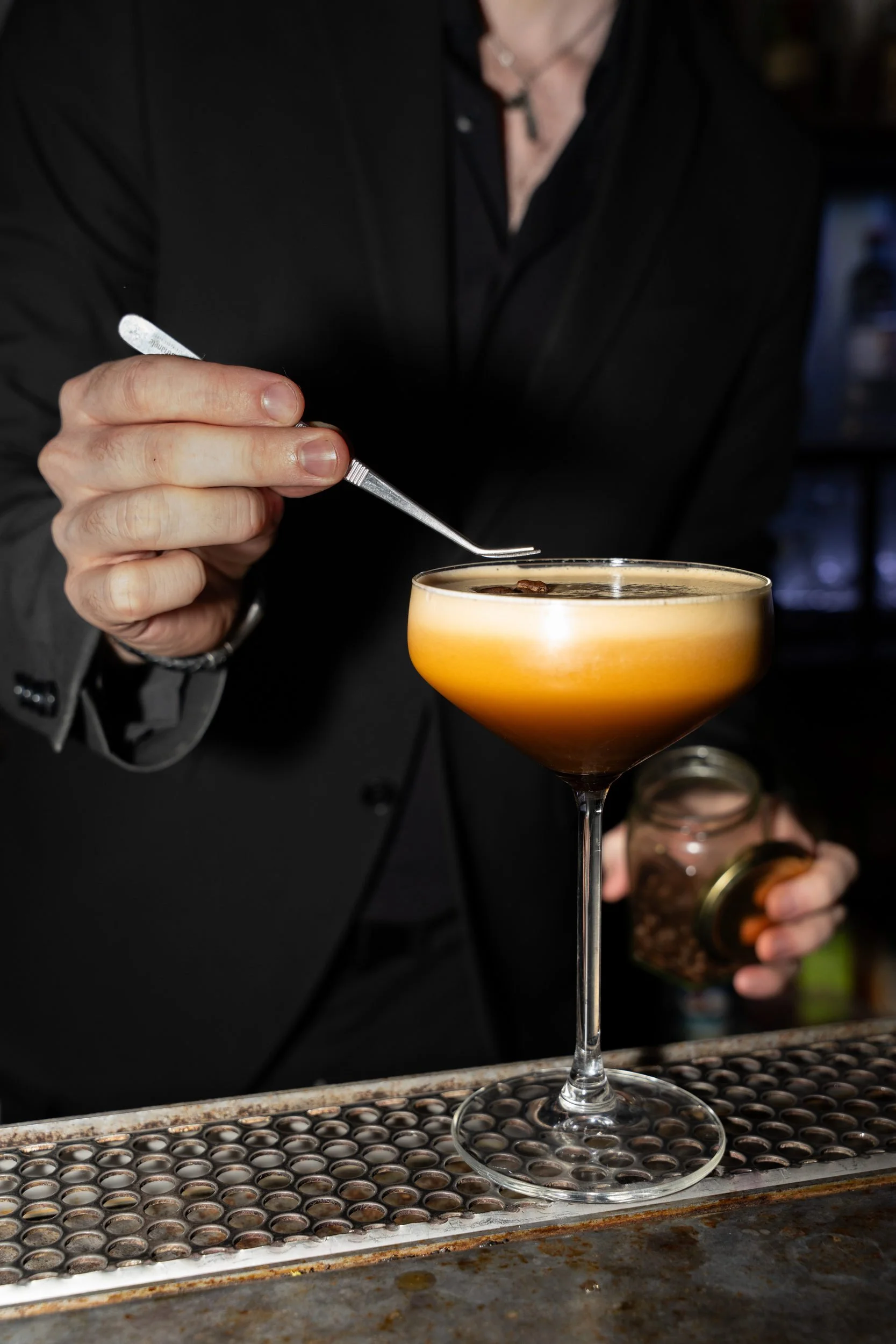 Bartender pynter en skummende cocktail i coupeglas med en pincet på Little Green Door