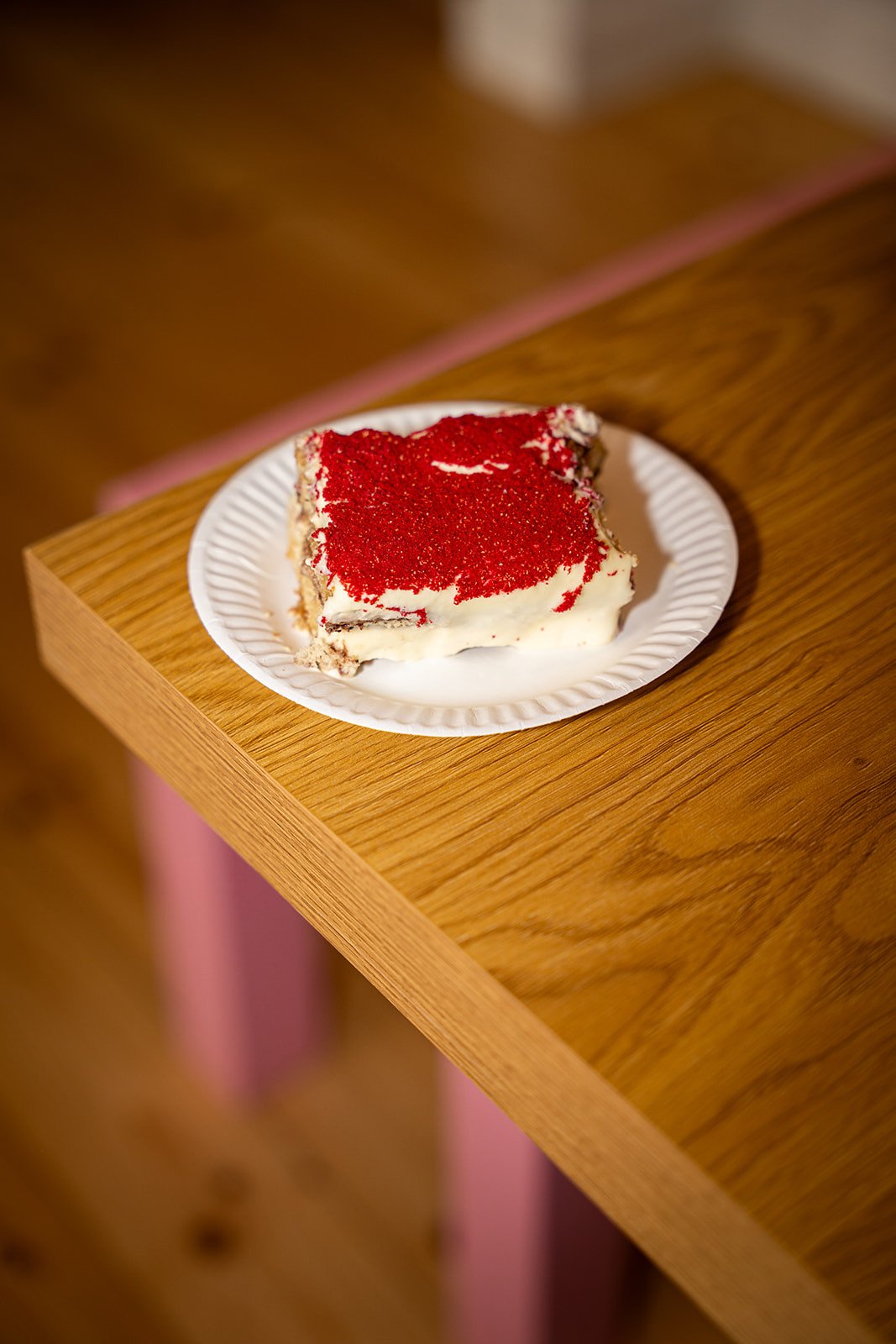 Tiramisu med rødt drys på en hvid tallerken på et træbord med lyserøde ben hos Flan