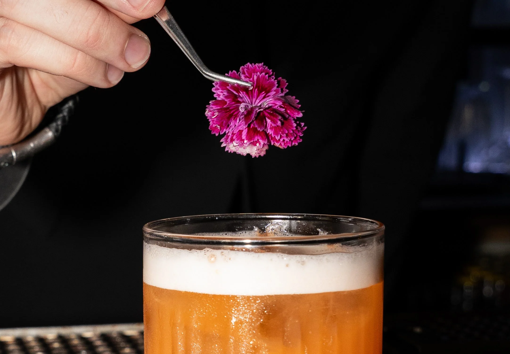Pink blomst lægges med pincet på en skummende cocktail hos Little Green Door København