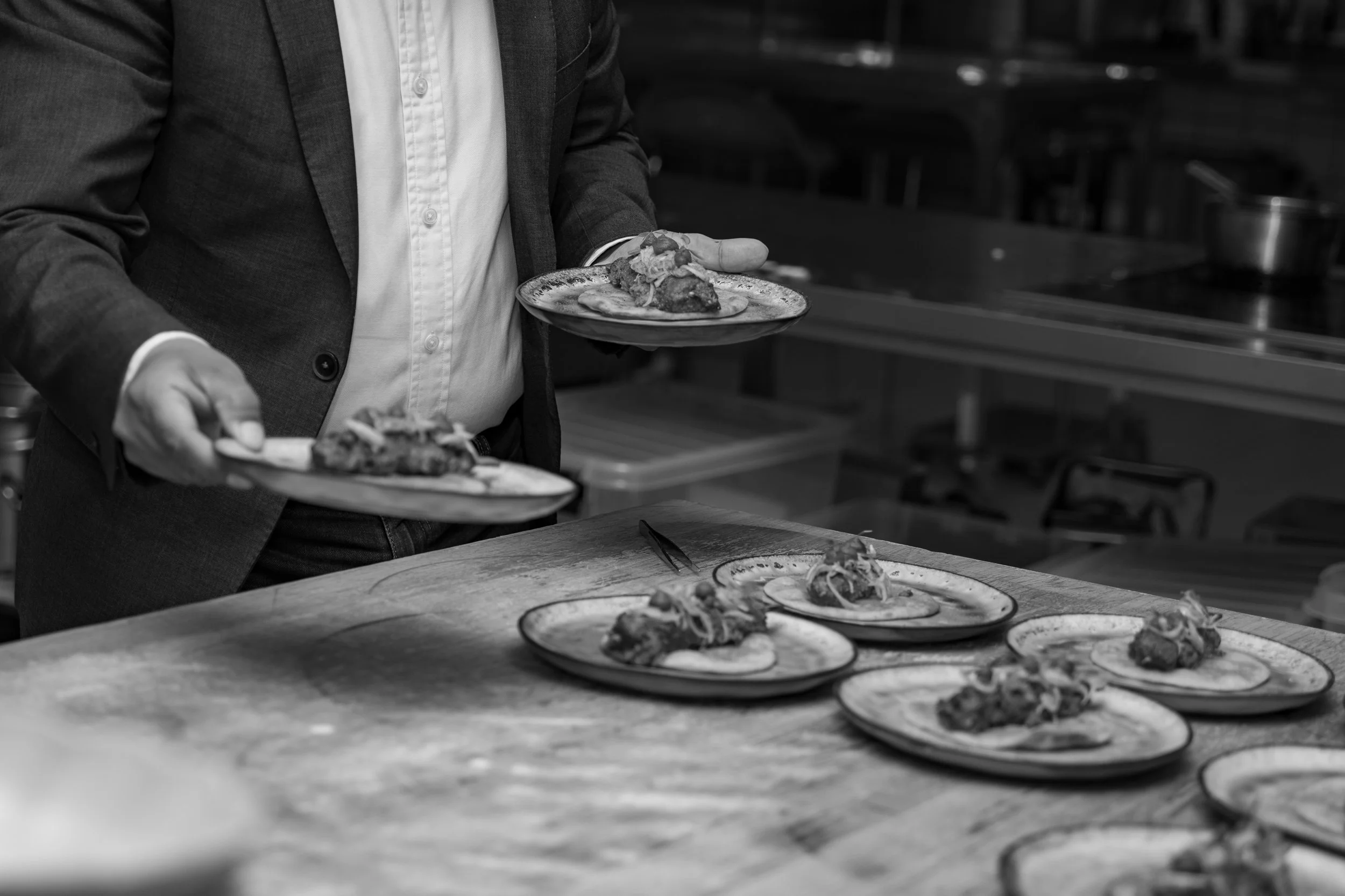 A man in a suit serving food on plates in a kitchen or dining area.