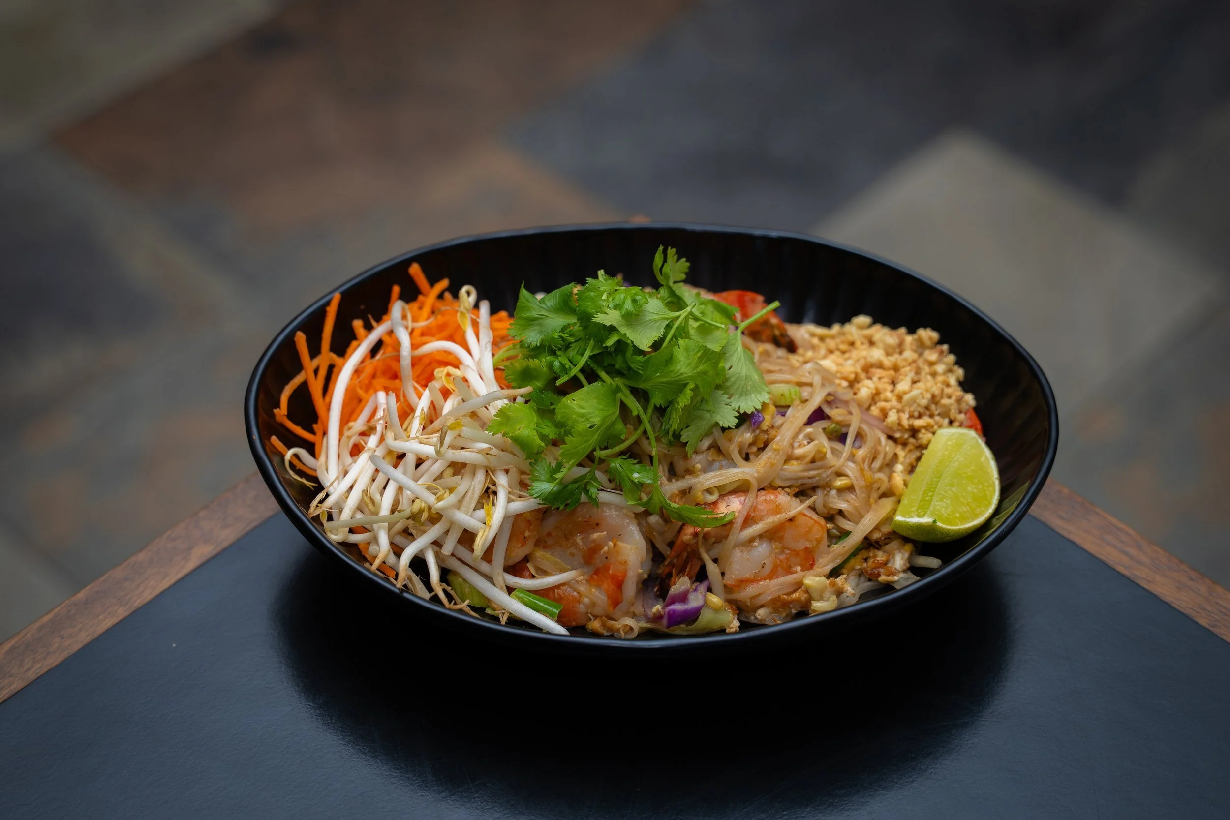 Thai noodle dish with fresh herbs and lime in a black bowl at WOK Copenhagen – restaurant photography by Monday's Photo