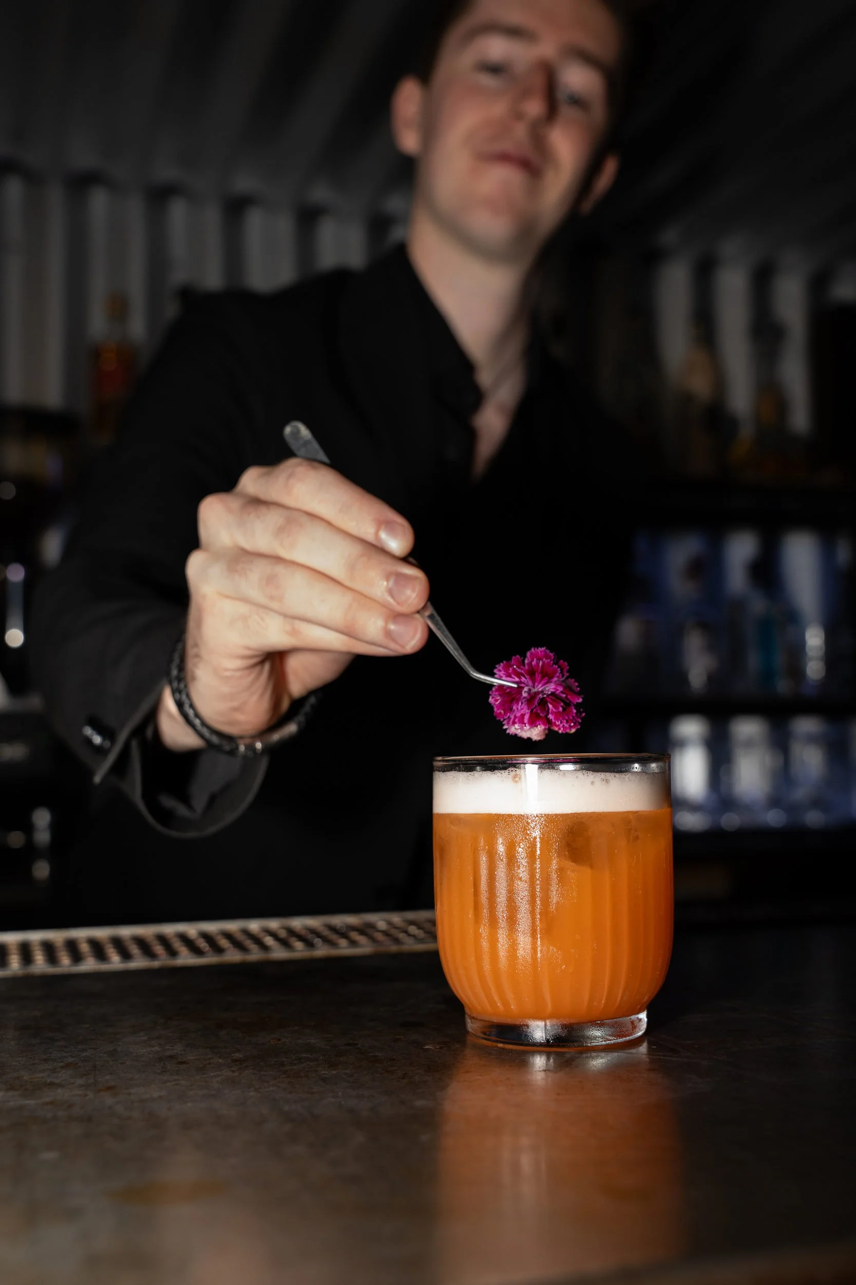 Bartender pynter en orange cocktail med en pink blomst på Little Green Door