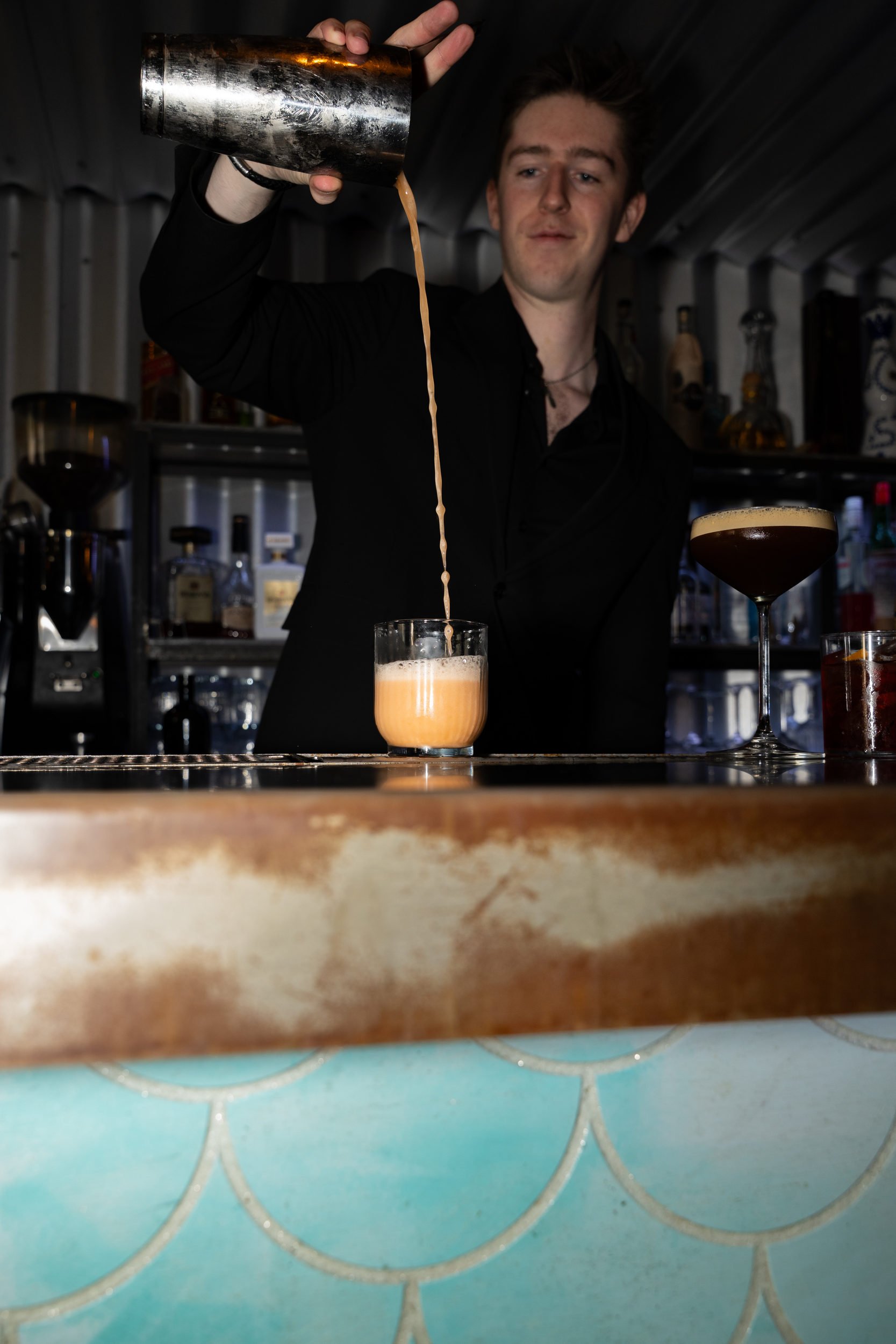Cocktail hældes fra shaker i et glas over den turkise bardisk på Little Green Door