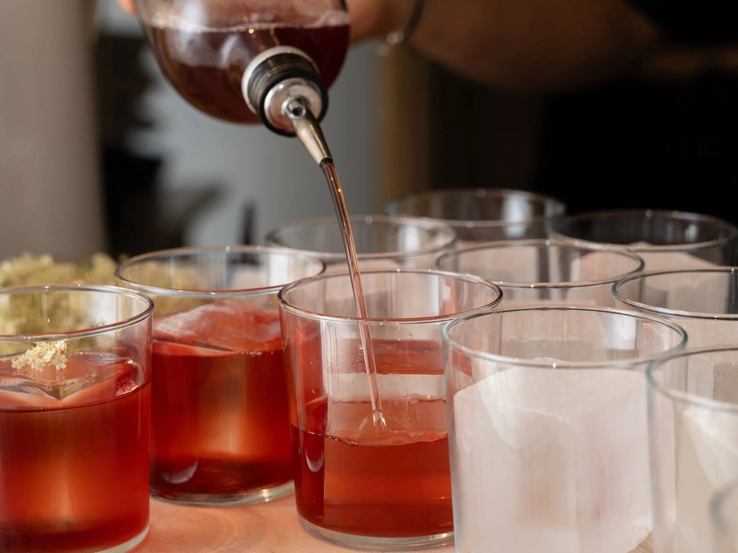 A close-up of several clear glass cups with pink liquid, with a dropper pouring pink liquid into one of the cups.