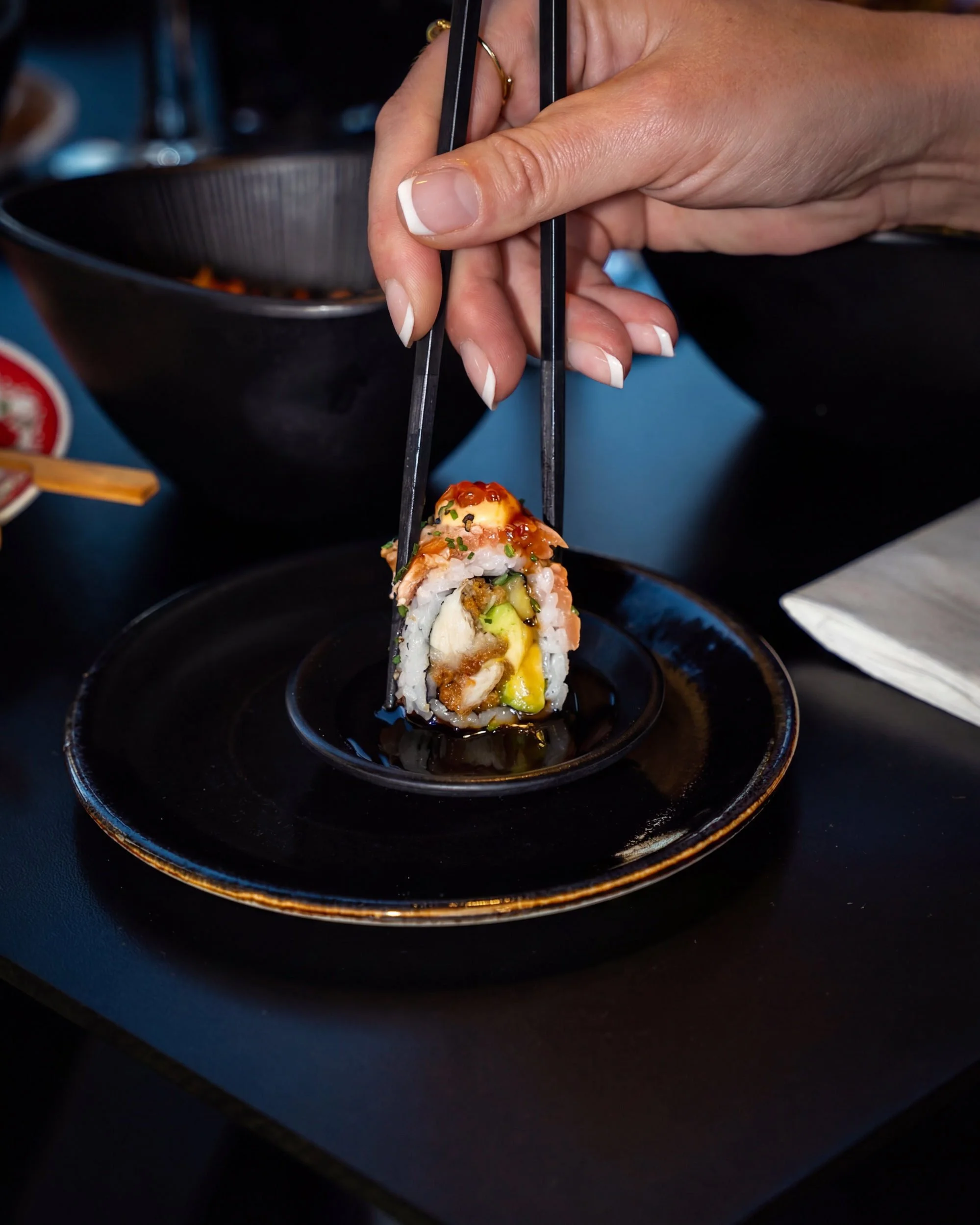 Spisepinde løfter en maki-rulle fra en sort tallerken hos Sushi Lab København