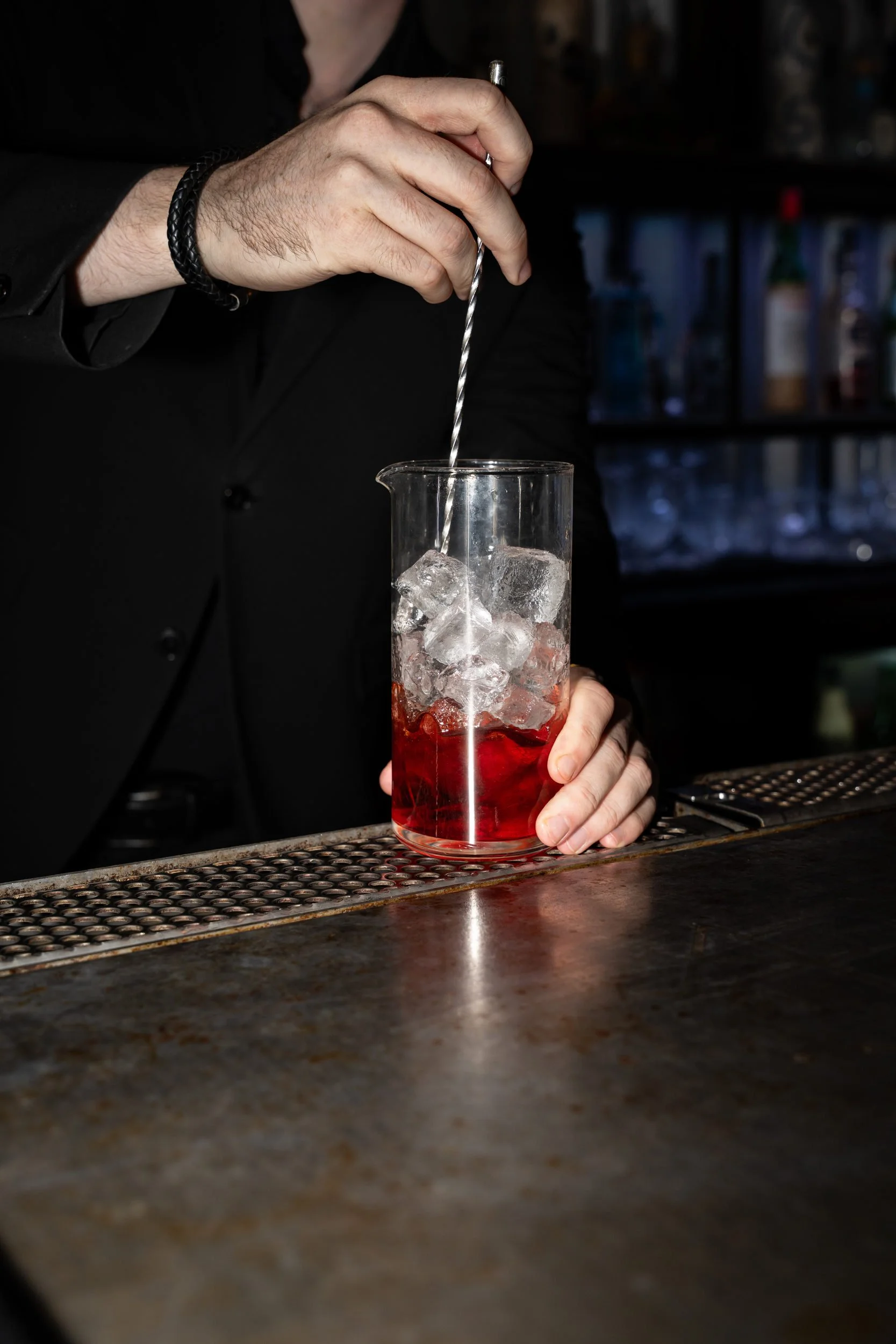 Bartender rører en rød cocktail i et røreglas på baren hos Little Green Door