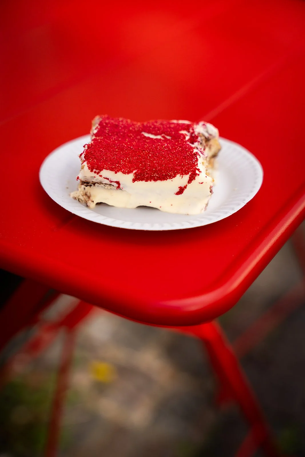 Stykke tiramisu med rødt drys på en hvid tallerken på et rødt cafébord ved Flan