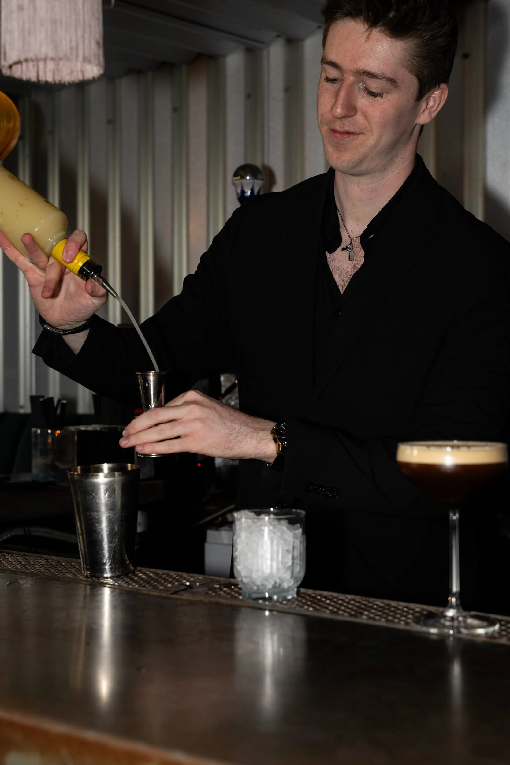 Bartender hælder op ved bardisken med en mørk cocktail klar ved siden af på Little Green Door