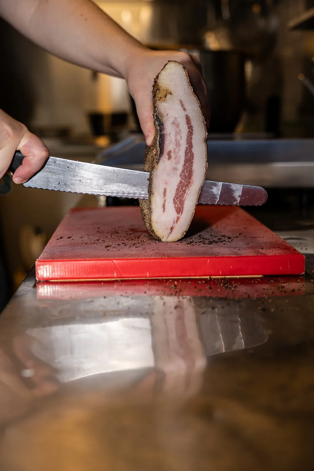 Guanciale skæres i skiver på et rødt skærebræt i køkkenet hos Il Mattarello