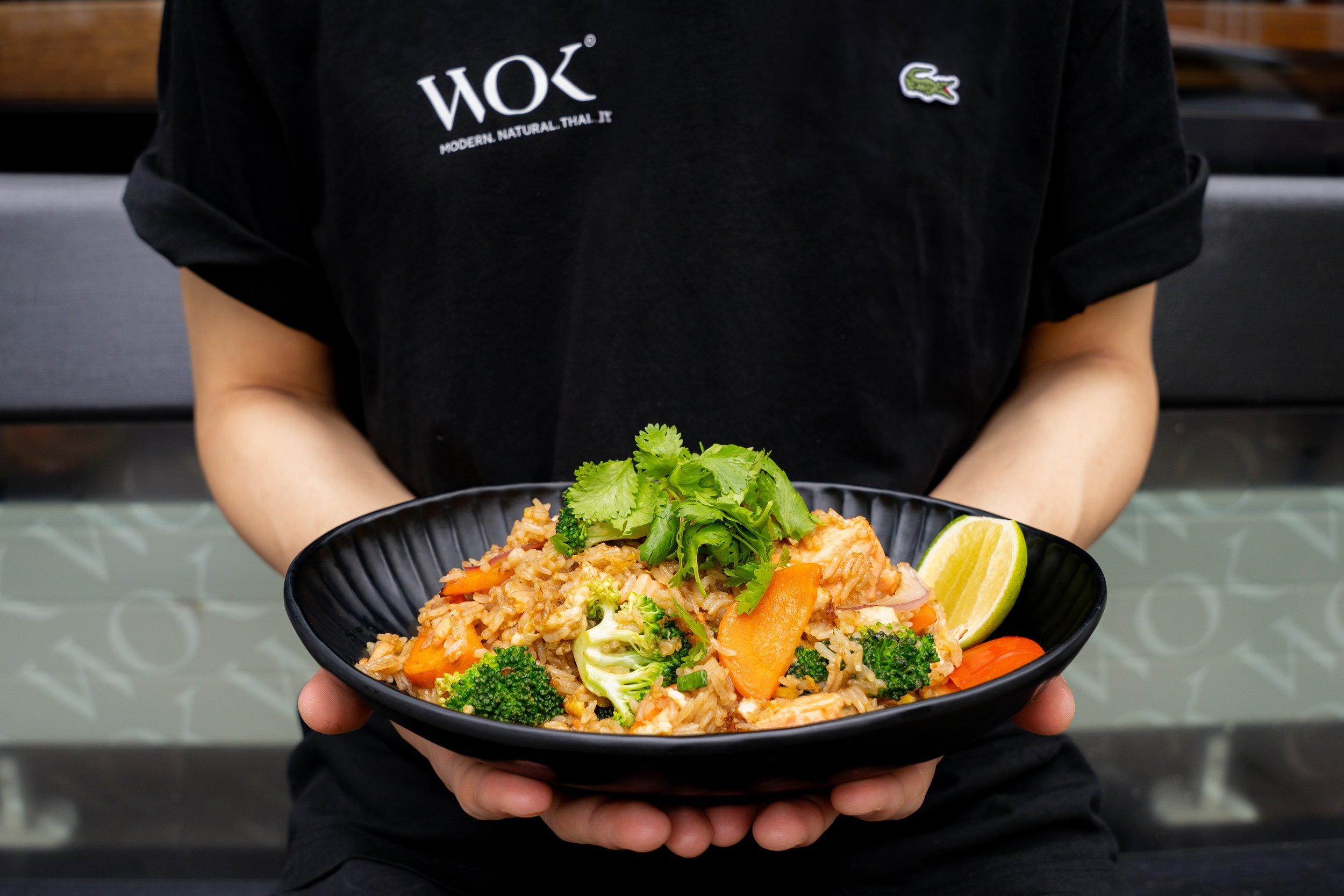 Hands holding a bowl of Thai wok dish with fresh herbs, team member in WOK apron at WOK Copenhagen – restaurant photography by Monday's Photo
