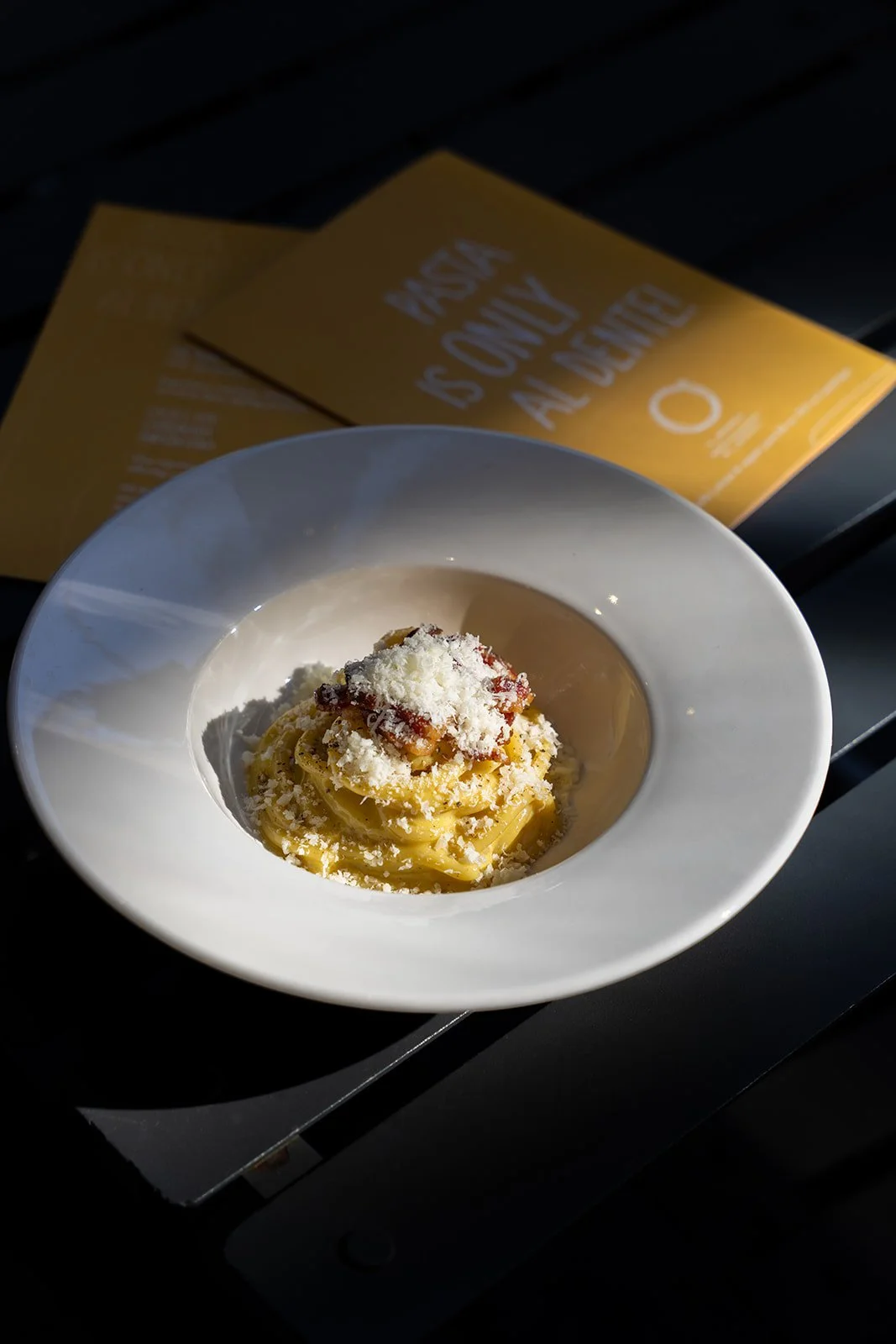 Carbonara med revet ost på en hvid tallerken ved et gult menukort hos Il Mattarello