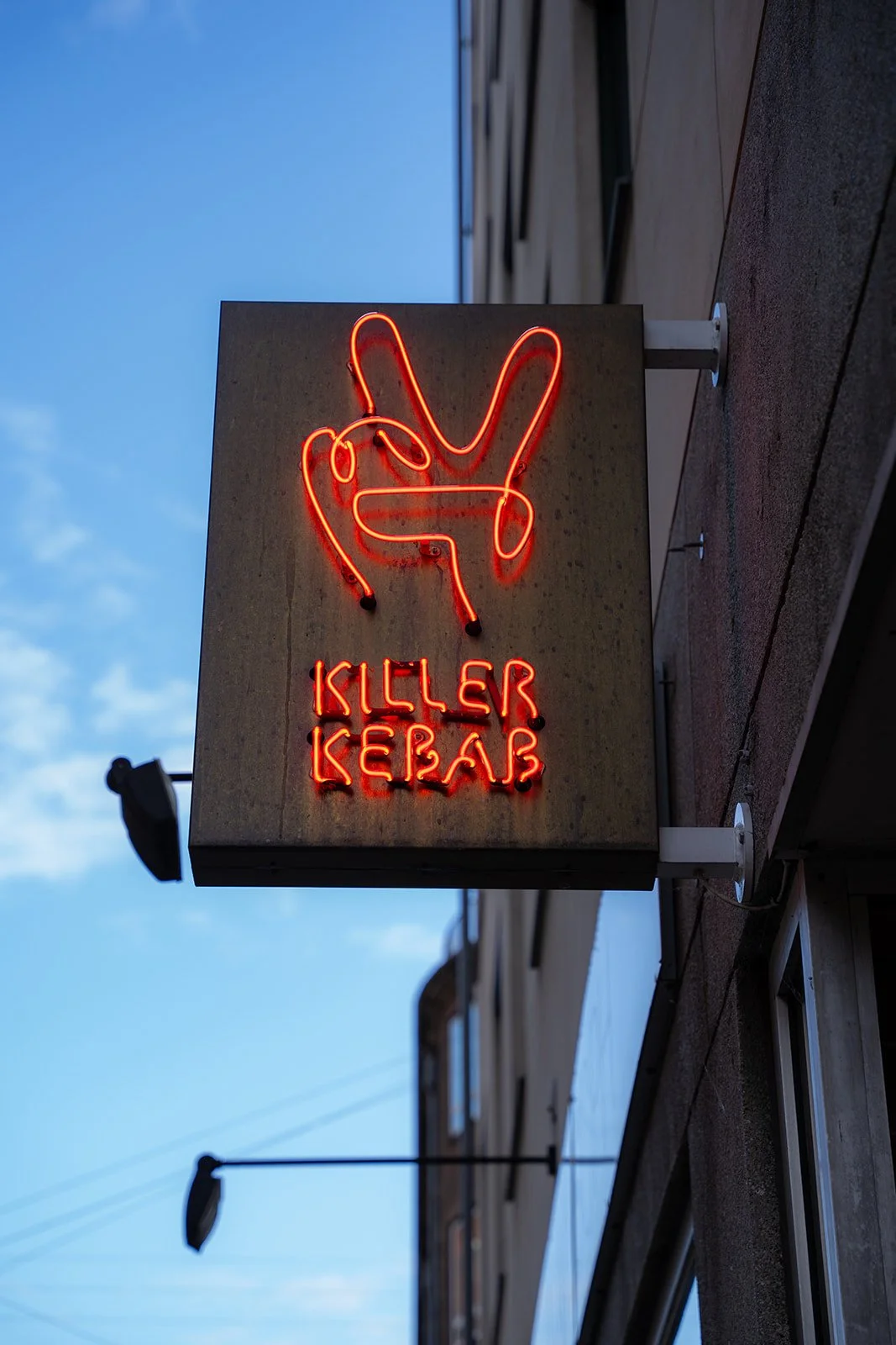 Killer Kebabs neonskilt med fredstegn hænger på facaden mod en blå himmel i København