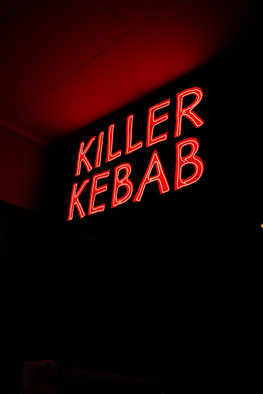 Rødt neonskilt med teksten Killer Kebab på en mørk væg inde i restauranten