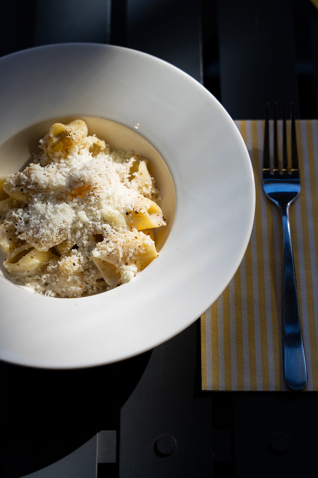 Rigatoni med revet pecorino i dyb hvid tallerken med gaffel på gul serviet hos Il Mattarello