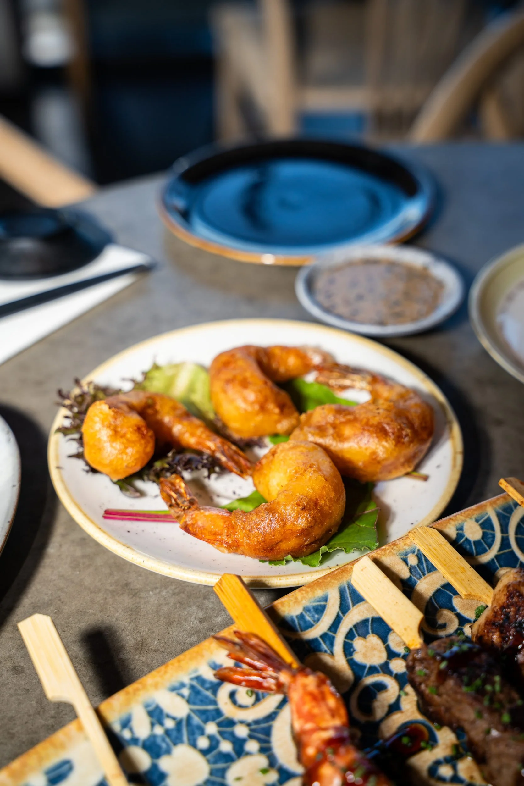 Sprødstegte rejer på hvid tallerken med grillede sticks i forgrunden hos Sushi Lab
