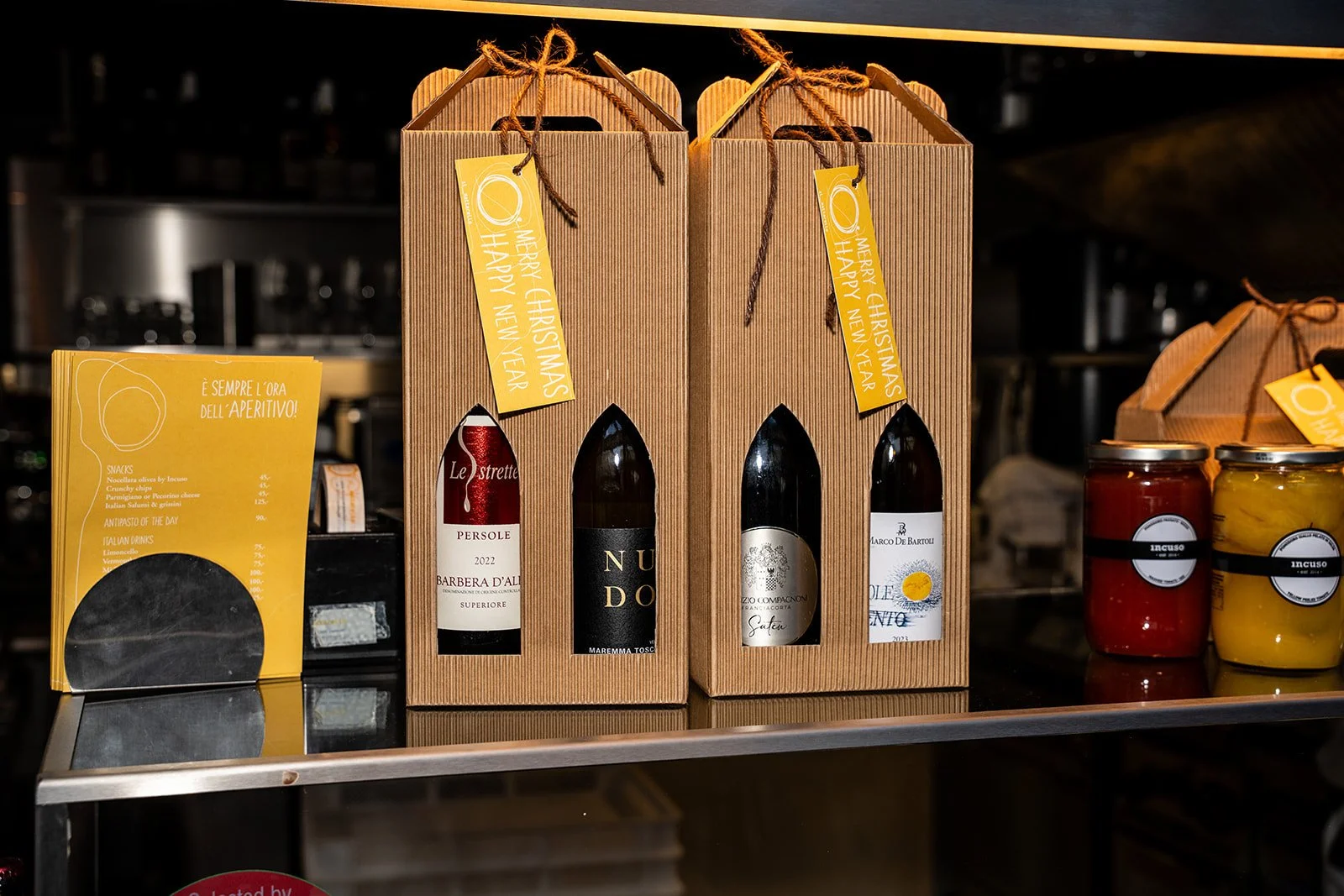Gaveæsker i pap med italiensk vin og glas med delikatesser på hylden hos Il Mattarello