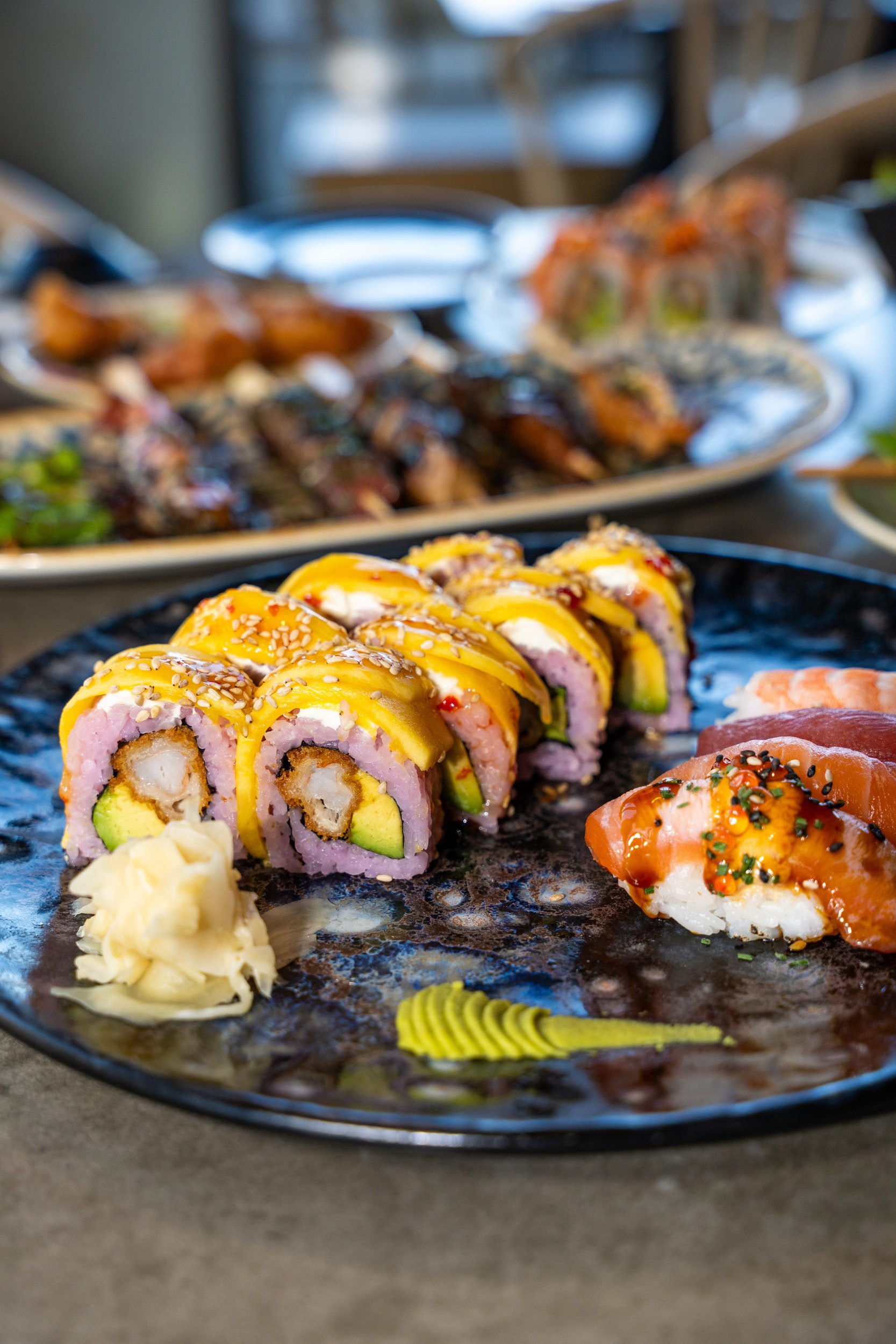 Maki-ruller med lyserødt sojapapir, gul topping og nigiri på sort fad hos Sushi Lab