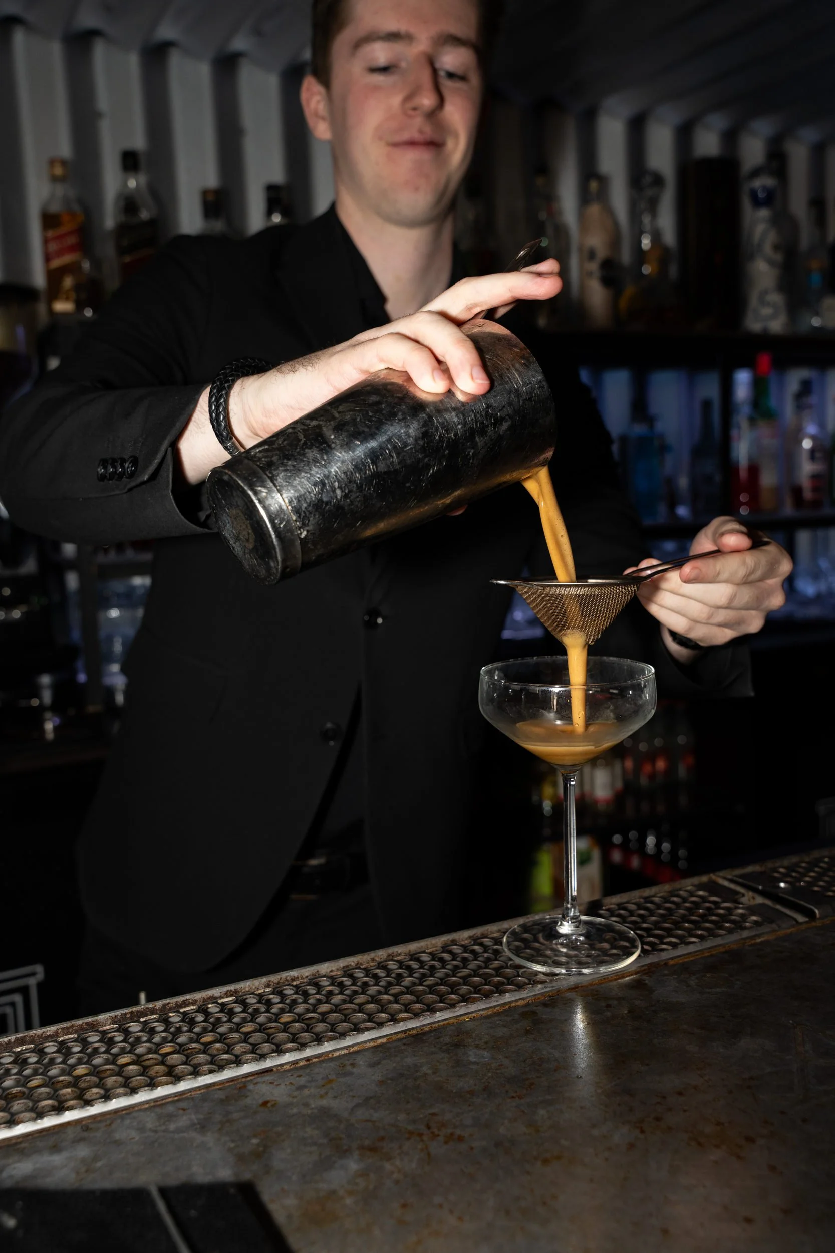 Bartender siler en cocktail fra shakeren i et coupeglas på Little Green Door København