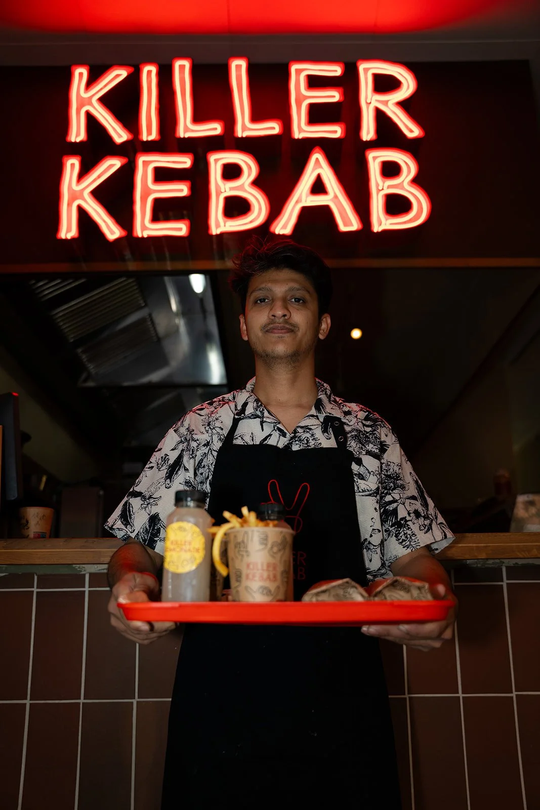 Medarbejder står med en fuld bakke mad under neonskiltet hos Killer Kebab