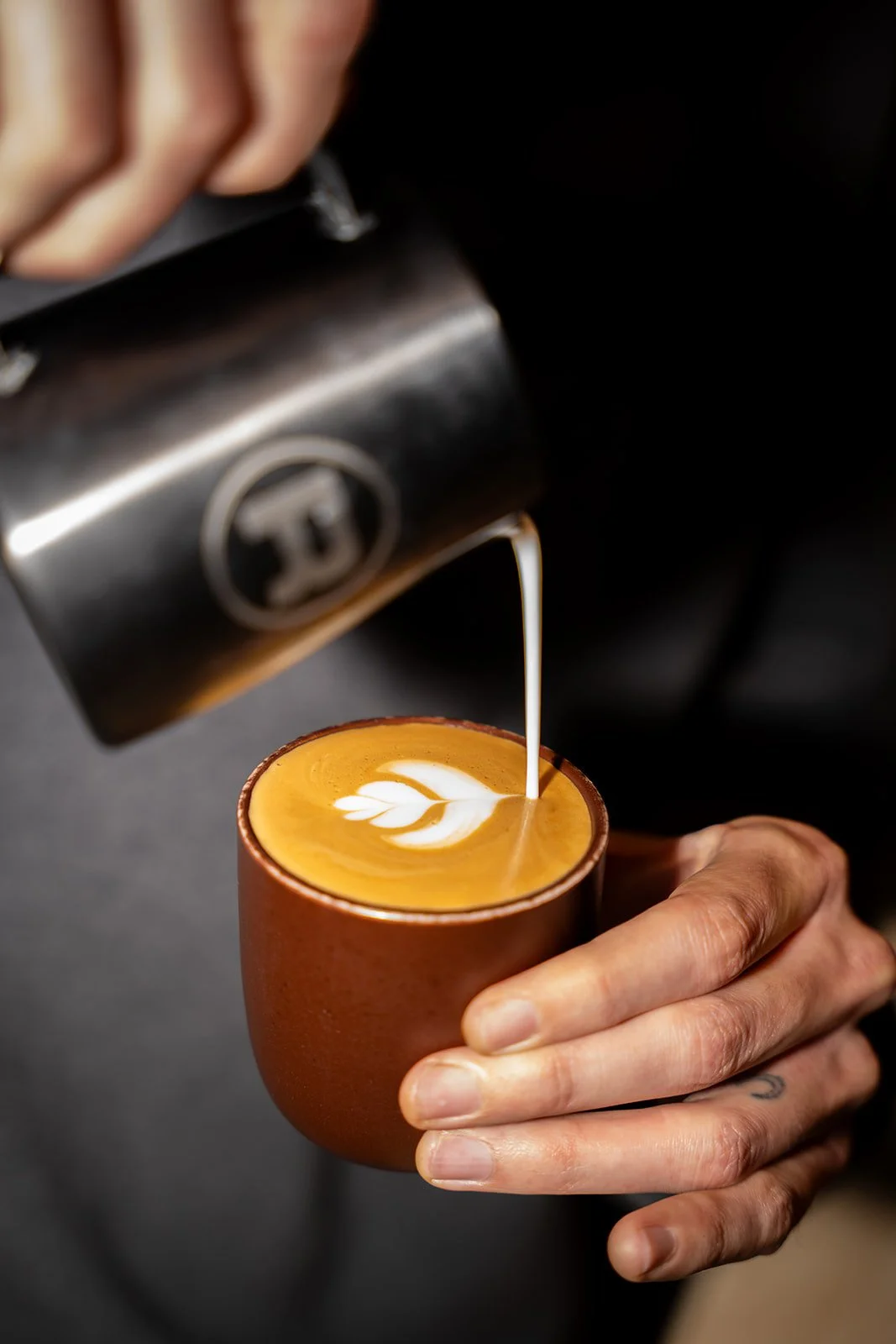 Latte art hældes i en brun kop hos Flan Arts & Coffee i København