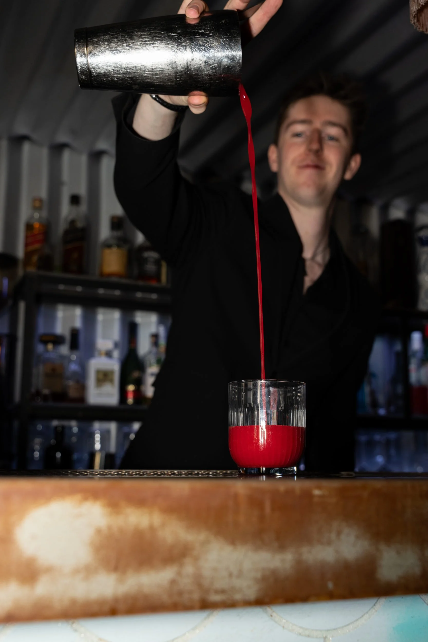 Rød cocktail hældes fra shaker i et glas over bardisken på Little Green Door