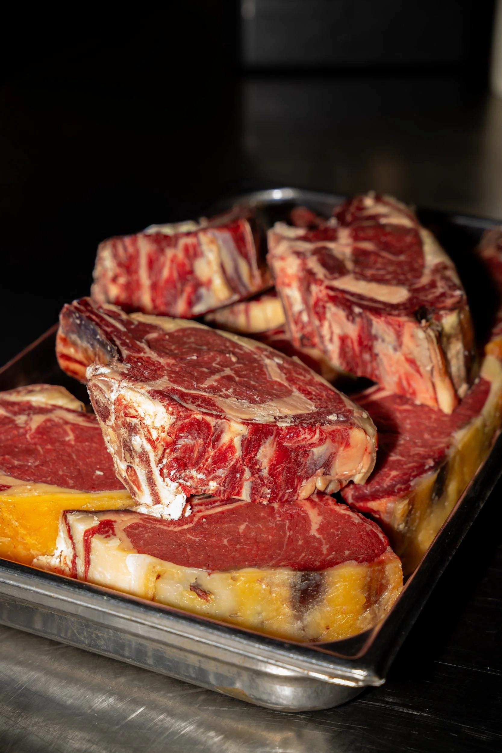 Store udskæringer af dry-aged oksekød med ben på en stålbakke hos A Hereford Beefstouw