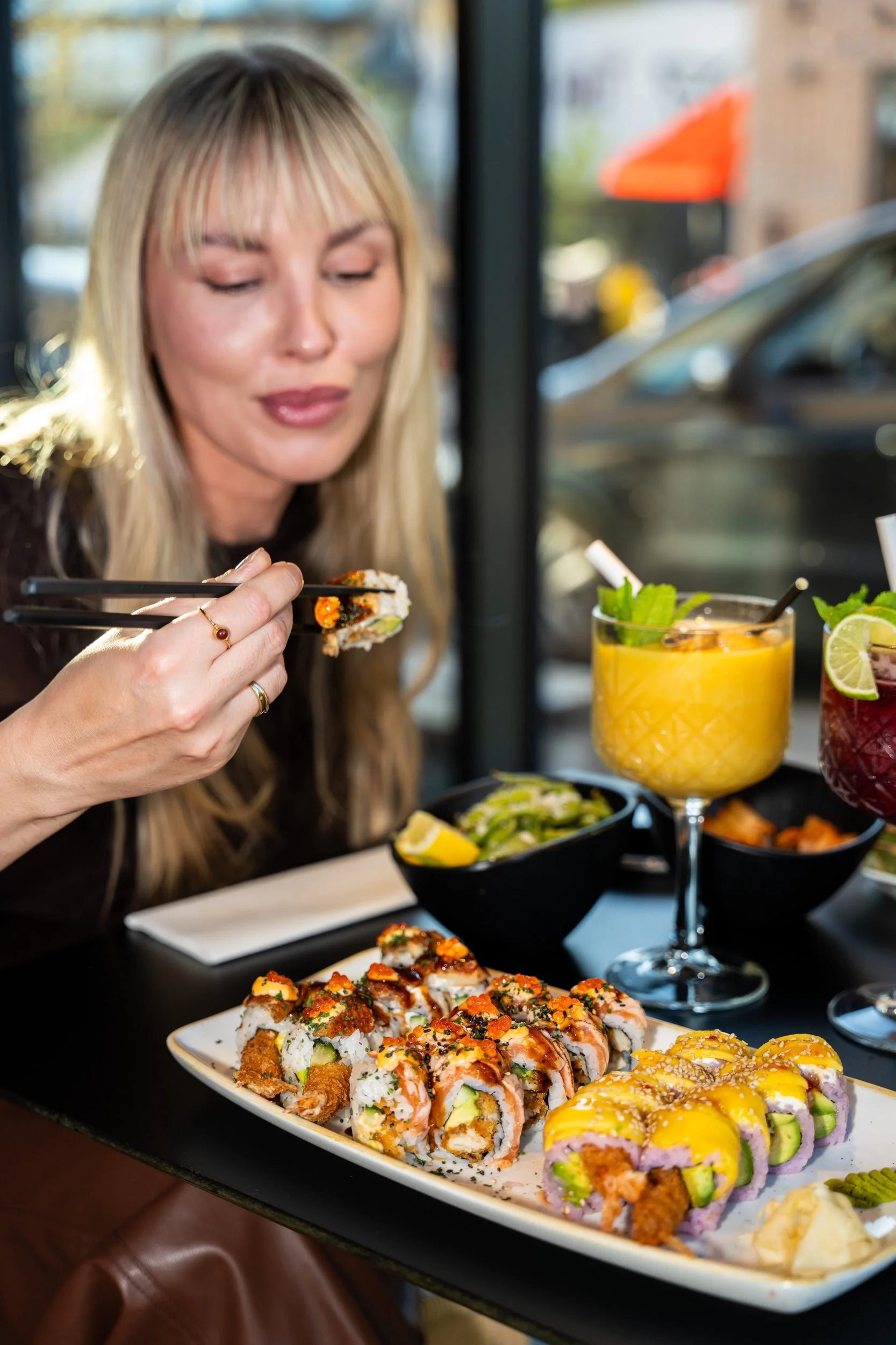 Gæst spiser sushi med spisepinde ved vinduesbordet med sushifad og cocktail hos Sushi Lab