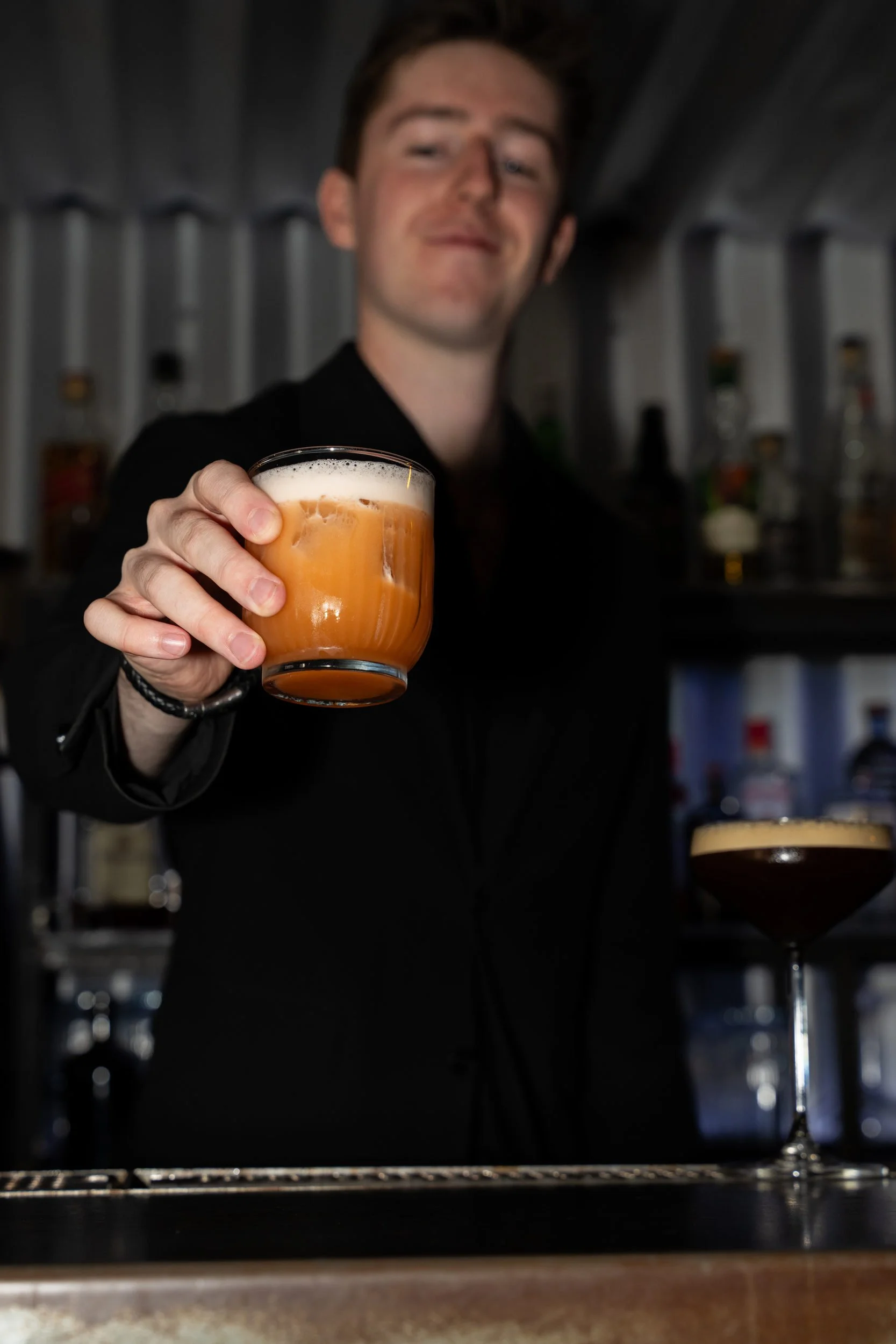 Bartender rækker en skummende orange cocktail frem på Little Green Door København