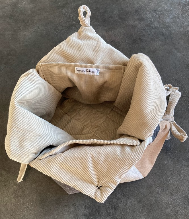 Un sac en tissu beige déplié, vue de dessus, avec une étiquette à l'intérieur portant le texte 'Temps Calme'.