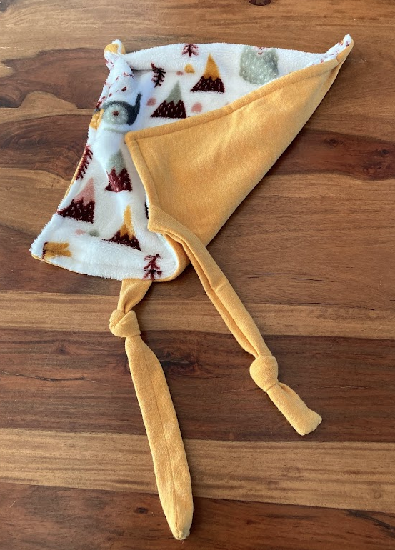 Doudou pour enfant en tissu doux, recto avec motif de montagnes enneigées et motif de sapins, verso en tissu jaune.