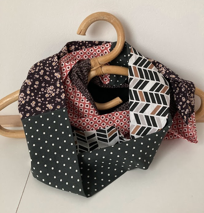 Écharpe en tissu avec différents motifs, accrochée à un cintre en bois.