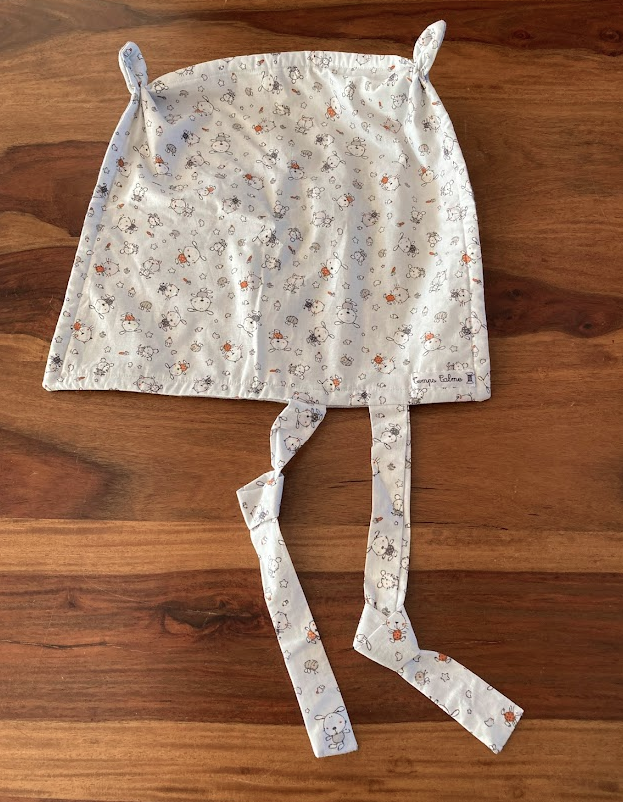 Doudou pour bébé en tissu blanc avec motifs d'ours et petits dessins, avec liens pour attacher la tétine.