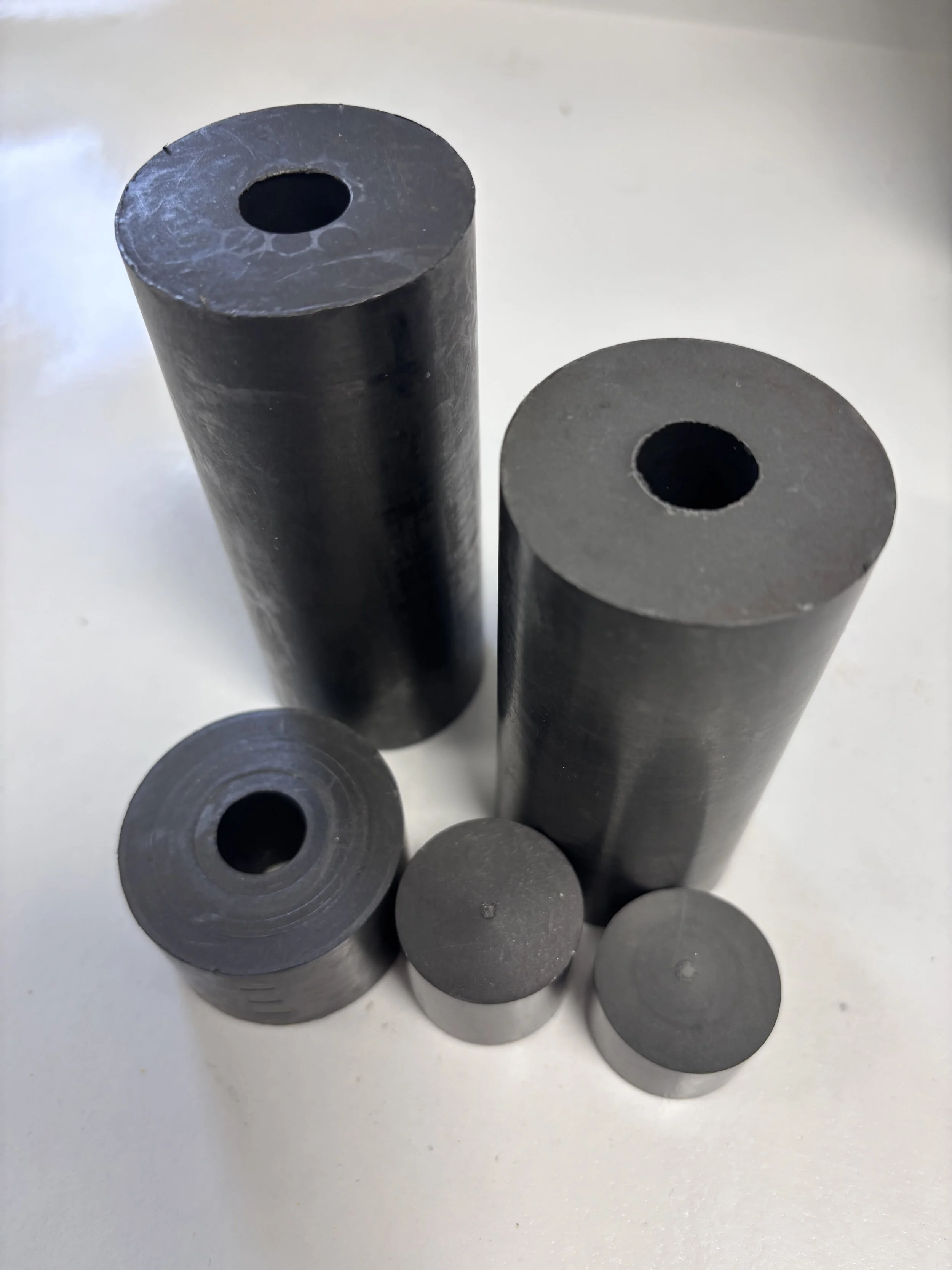 Five black rubber or plastic cylinders of varying heights and diameters with hollow centers, placed on a white surface.